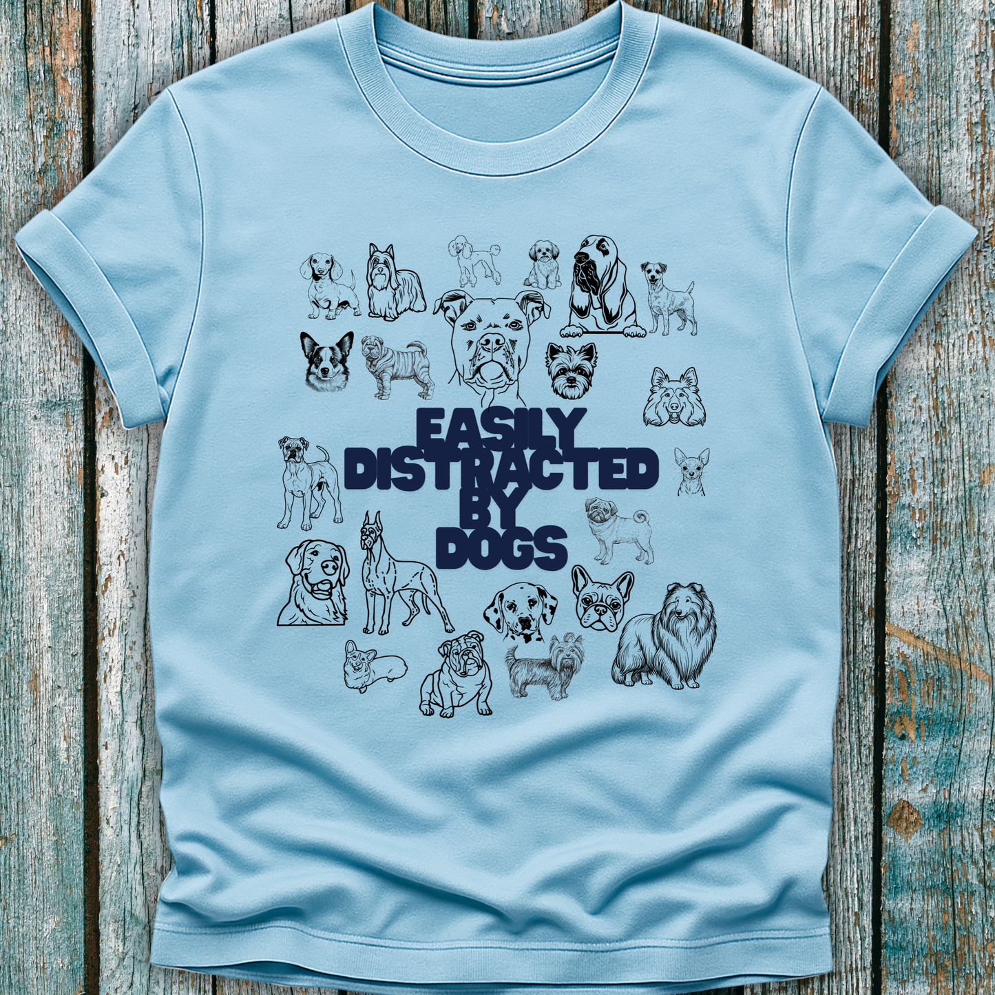 Light blue t-shirt with black dog illustrations and 'Easily Distracted by Dogs' text on a wooden surface.