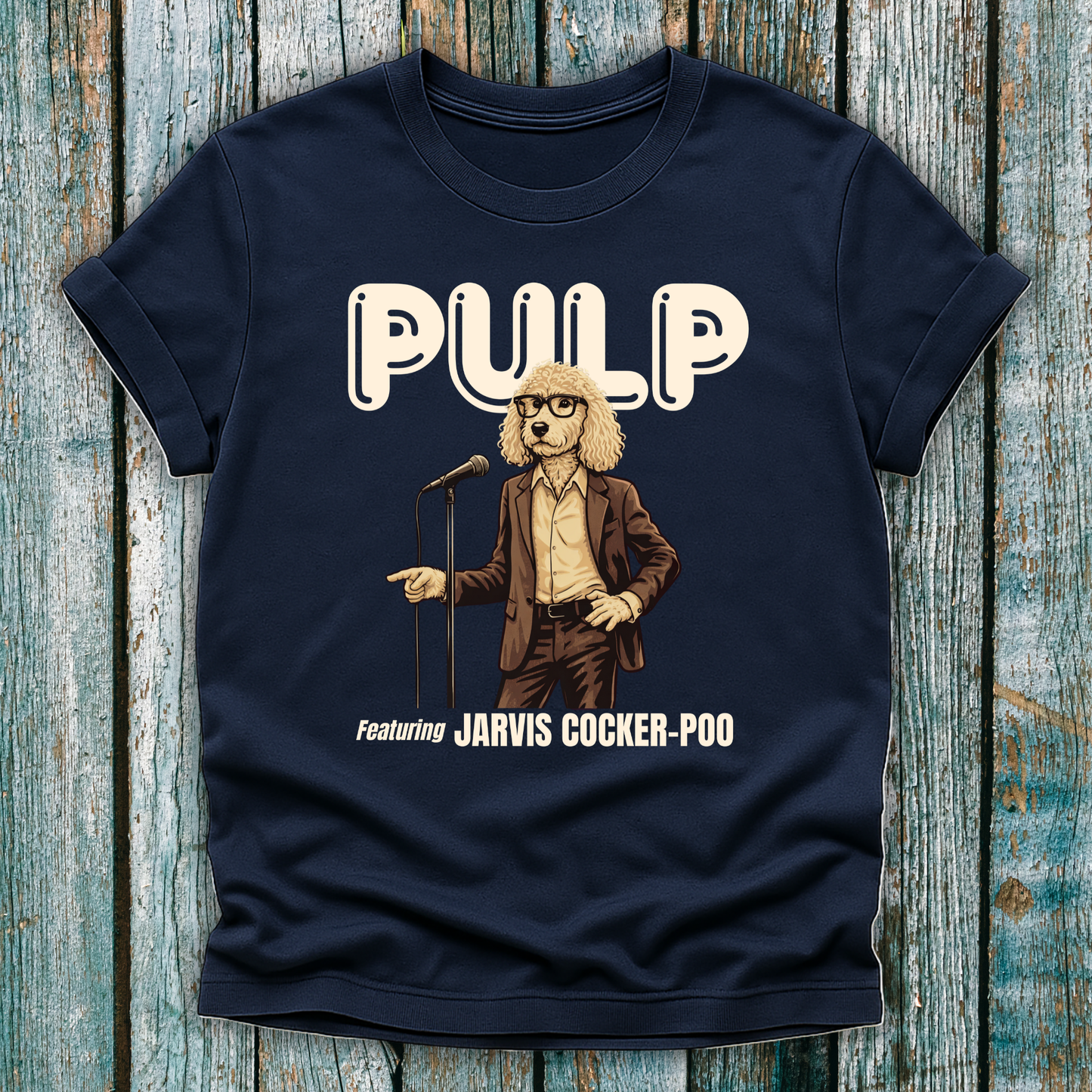 Navy blue t-shirt with a graphic of a dog in a suit and glasses holding a microphone, labeled 'Pulp featuring Jarvis Cocker Poo', on a wooden surface.