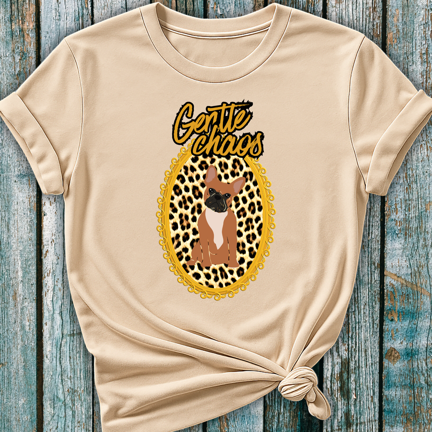 Beige t-shirt with a graphic of a Frenchie dog in a leopard print frame and 'Gentle Chaos' text, on a wooden surface.
