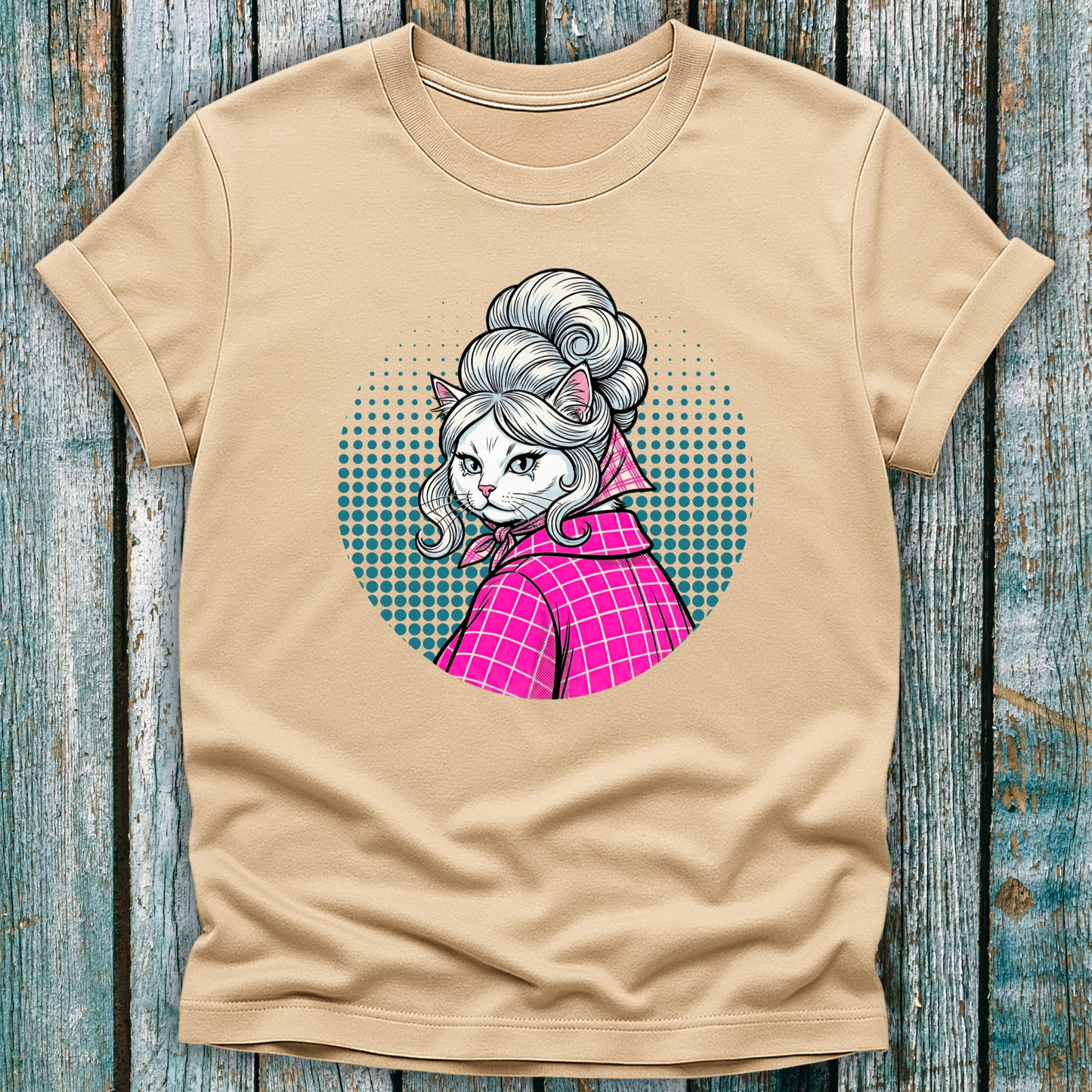 Beige t-shirt with a colorful graphic of a pop art cat character in a pink outfit on a wooden surface