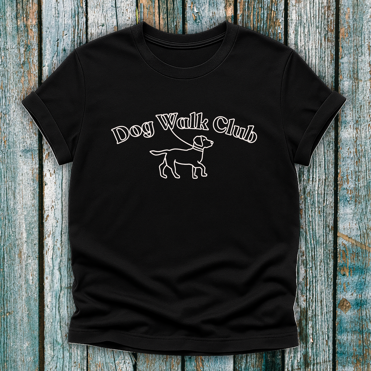 Black t-shirt with 'Dog Walk Club' text and dog illustration on a wooden surface