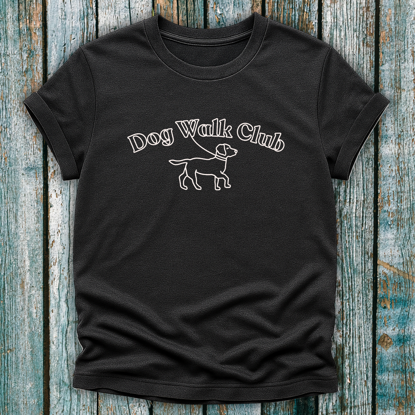 Black t-shirt with 'Dog Walk Club' text and dog illustration on a wooden surface