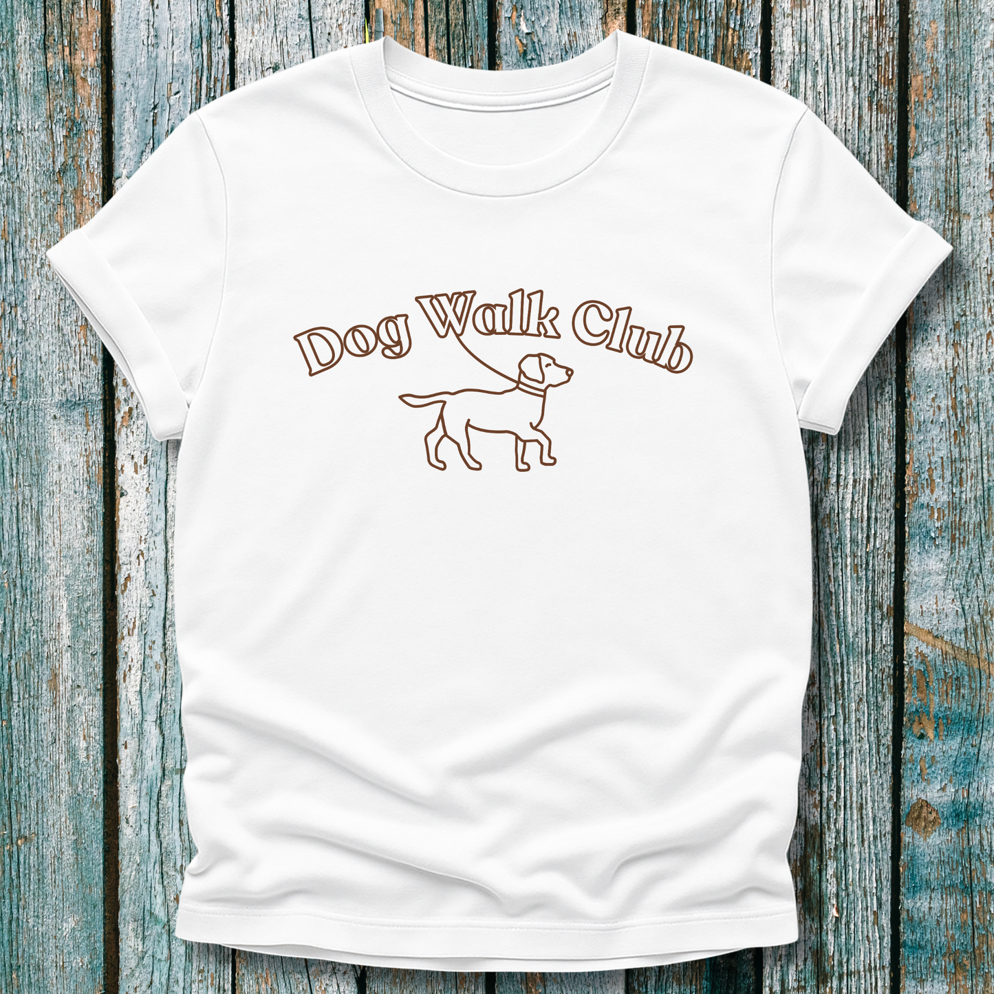 White t-shirt with 'Dog Walk Club' text and dog illustration on a wooden background