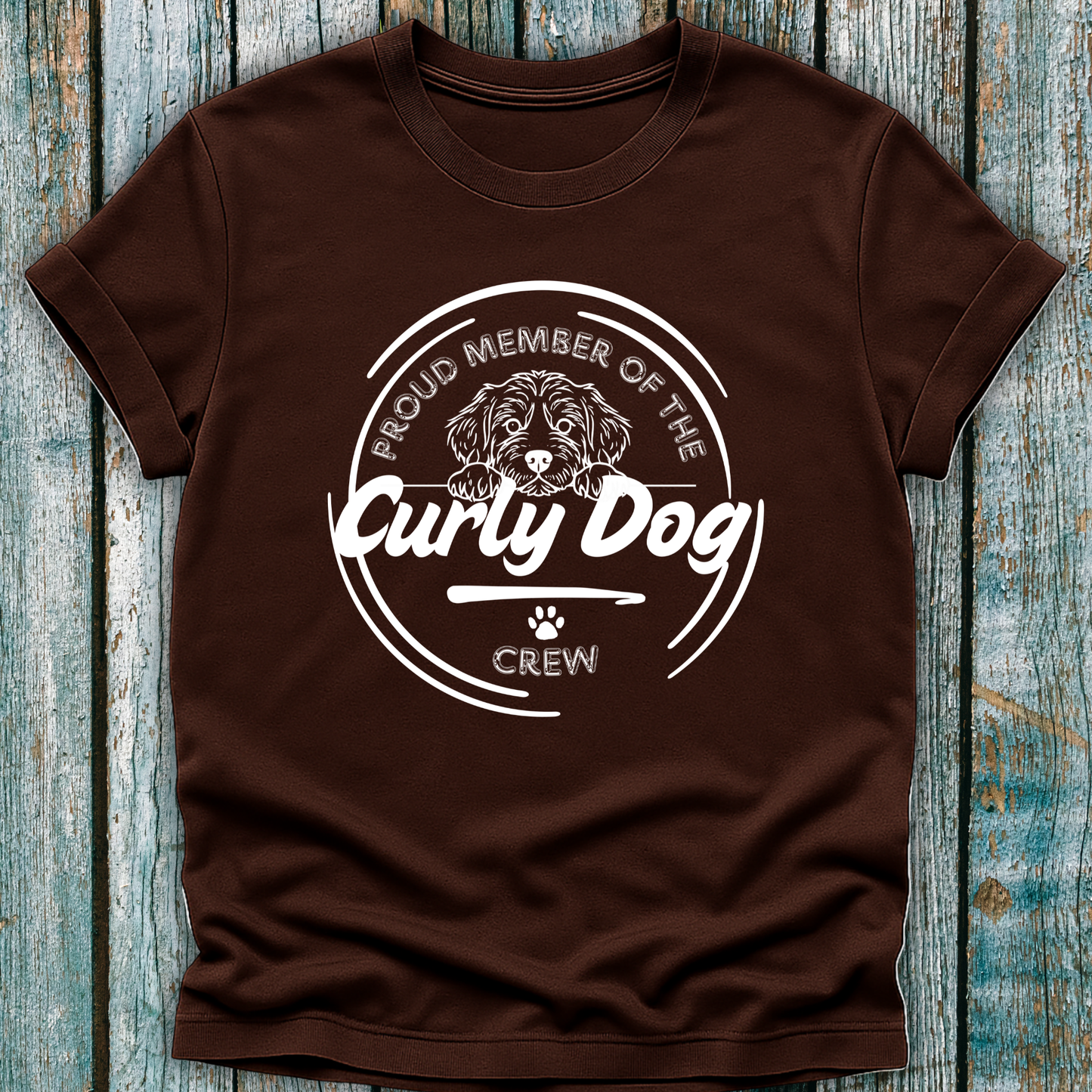Brown t-shirt with 'Proud Member of the Curly Dog Crew' graphic on a wooden surface