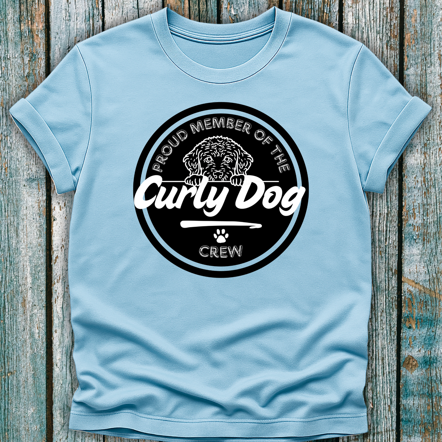 Light blue t-shirt with 'Proud Member of the Curly Dog Crew' graphic on a wooden surface