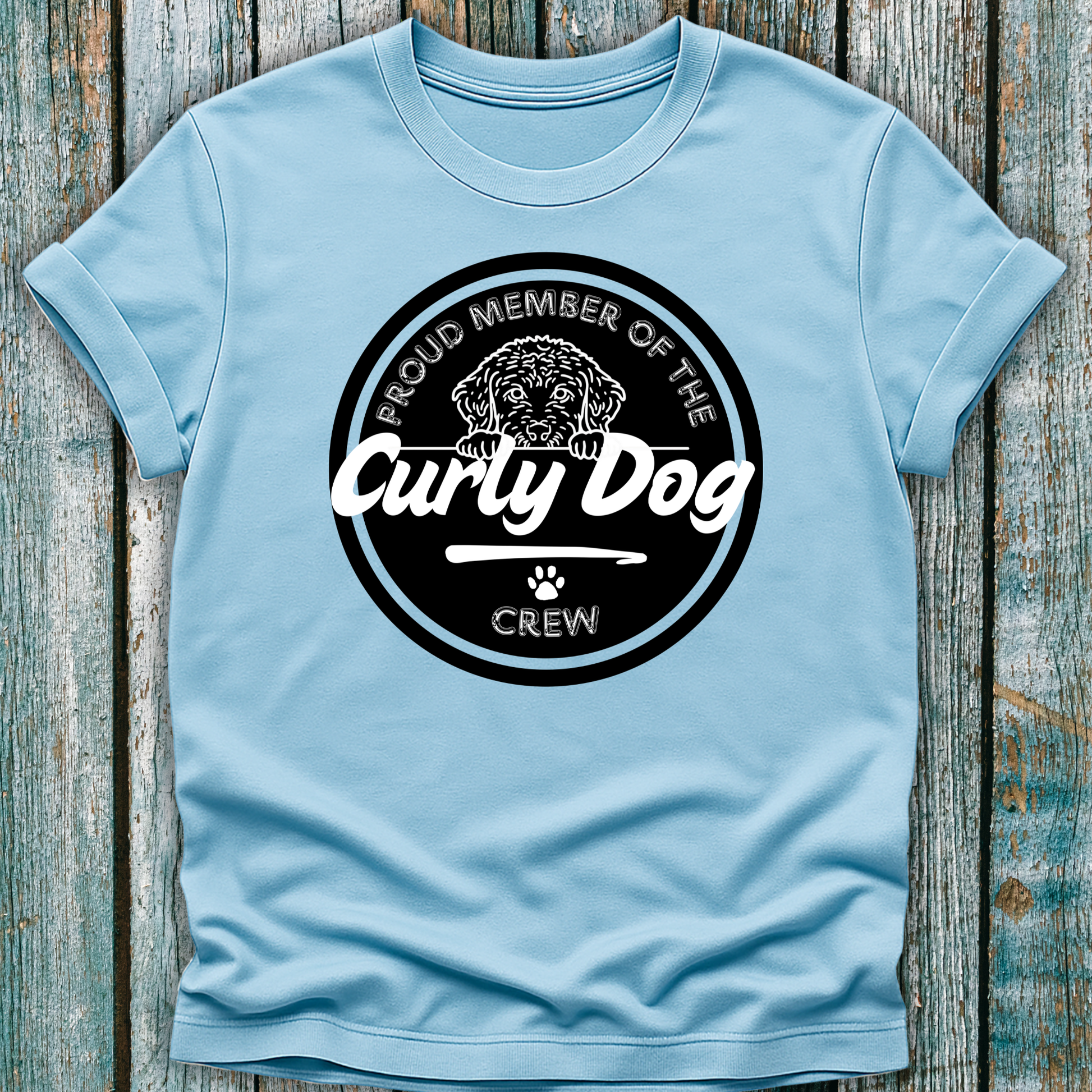 Light blue t-shirt with 'Proud Member of the Curly Dog Crew' graphic on a wooden surface