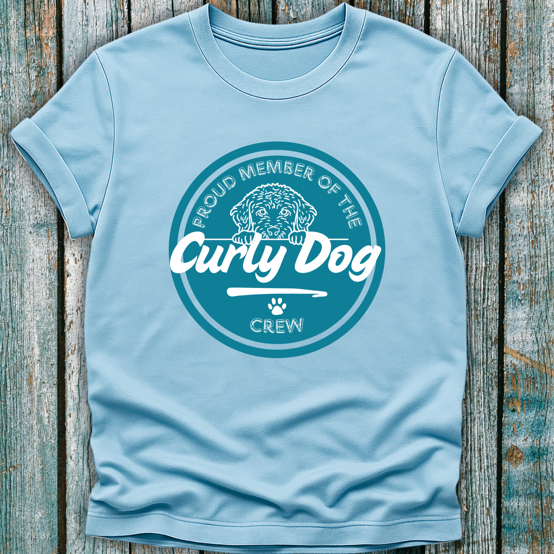 Light blue t-shirt with 'Proud Member of the Curly Dog Crew' design on a wooden surface