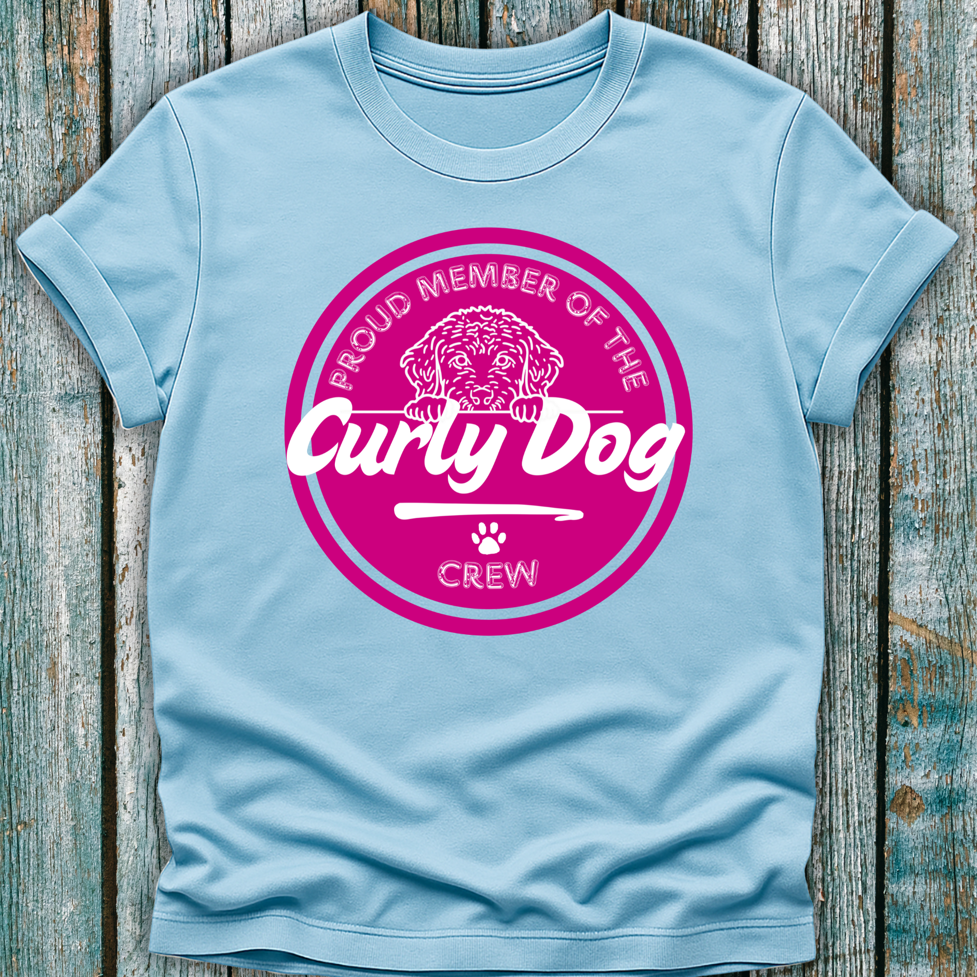 Light blue t-shirt with pink 'Proud Member of the Curly Dog Crew' graphic on a wooden surface