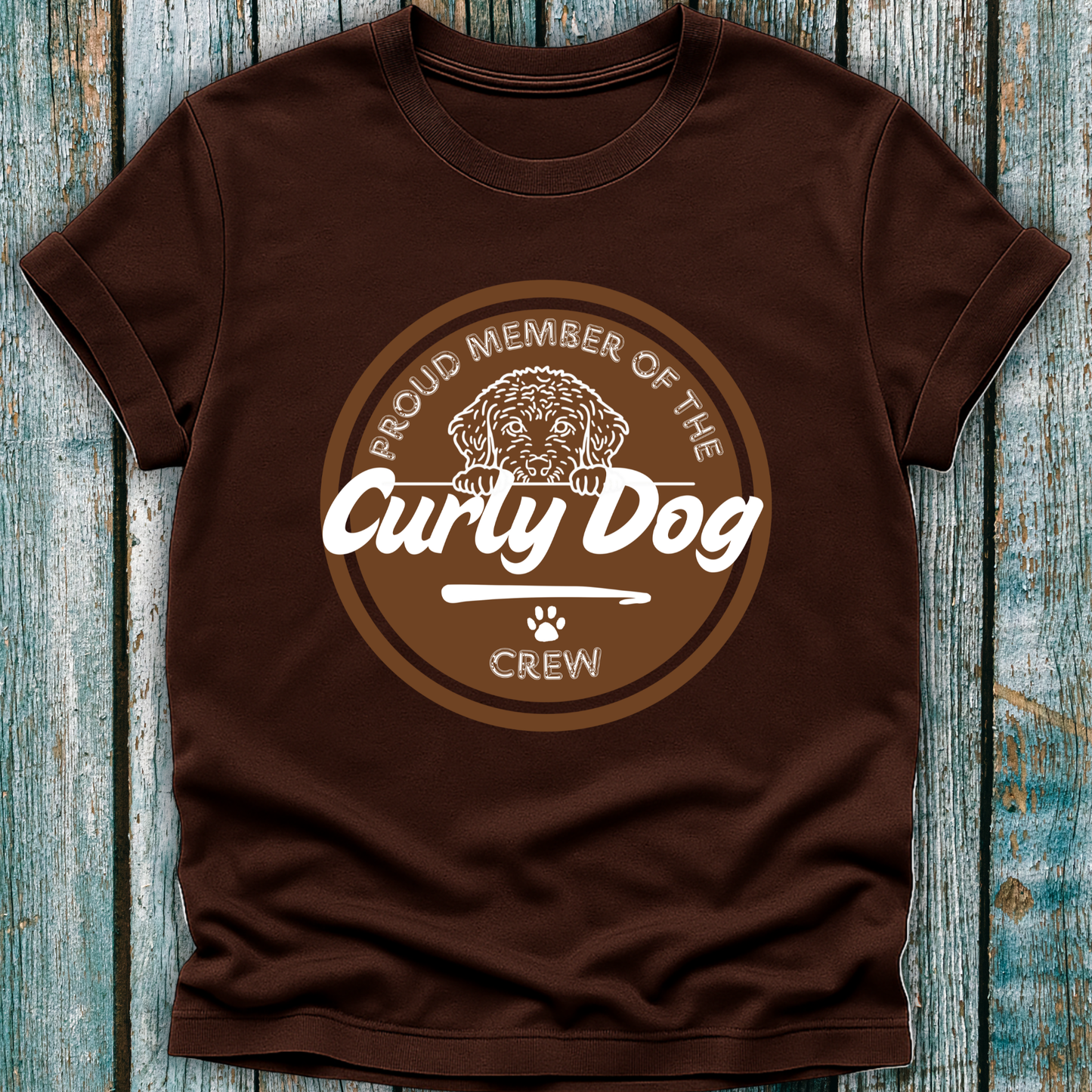 Brown t-shirt with 'Proud Member of the Curly Dog Crew' graphic on a wooden surface