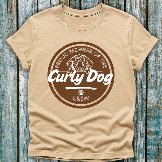 Beige t-shirt with 'Proud Member of the Curly Dog Crew' graphic on a wooden surface