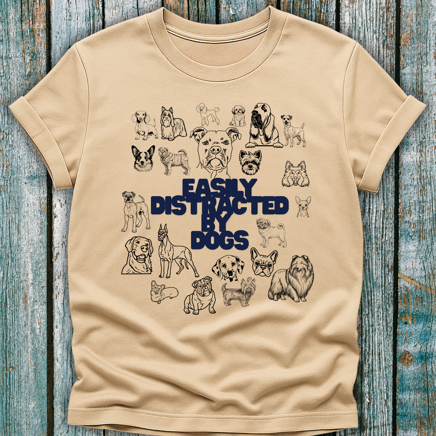 Beige t-shirt with dog illustrations and 'Easily Distracted by Dogs' text on a wooden surface