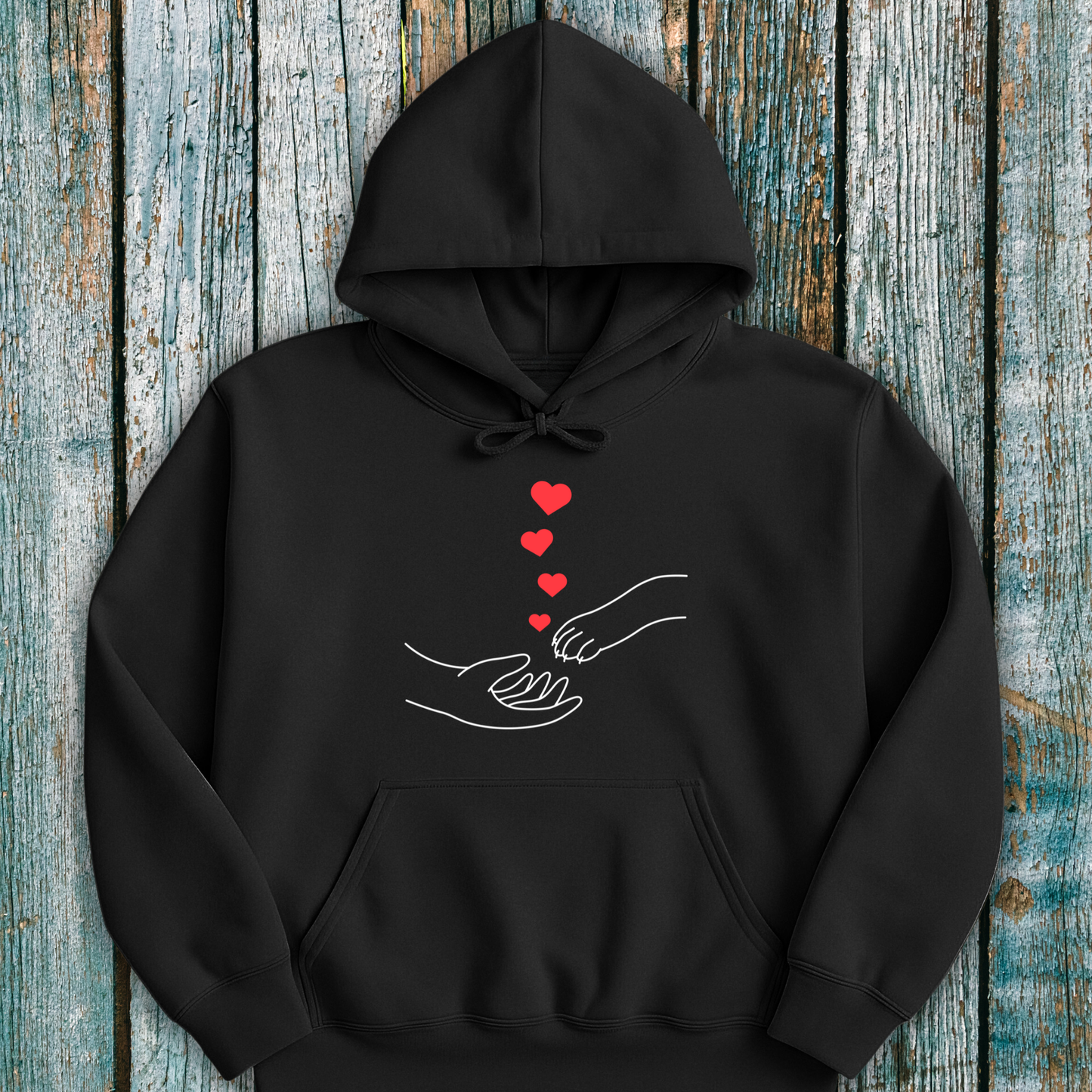 Black hoodie with a design of hands holding paws and hearts on a wooden surface