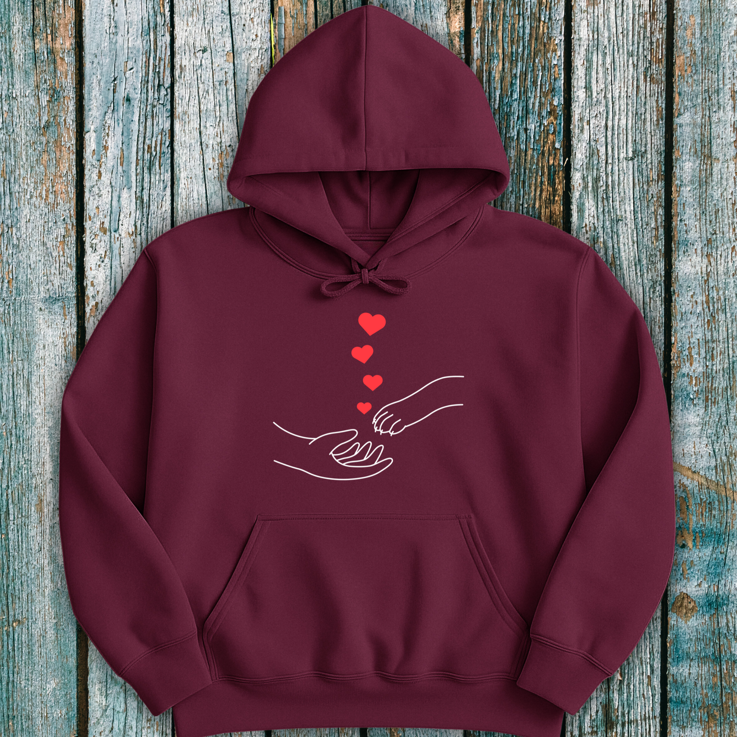 Maroon hoodie with a design of hands holding paws and hearts on a wooden surface
