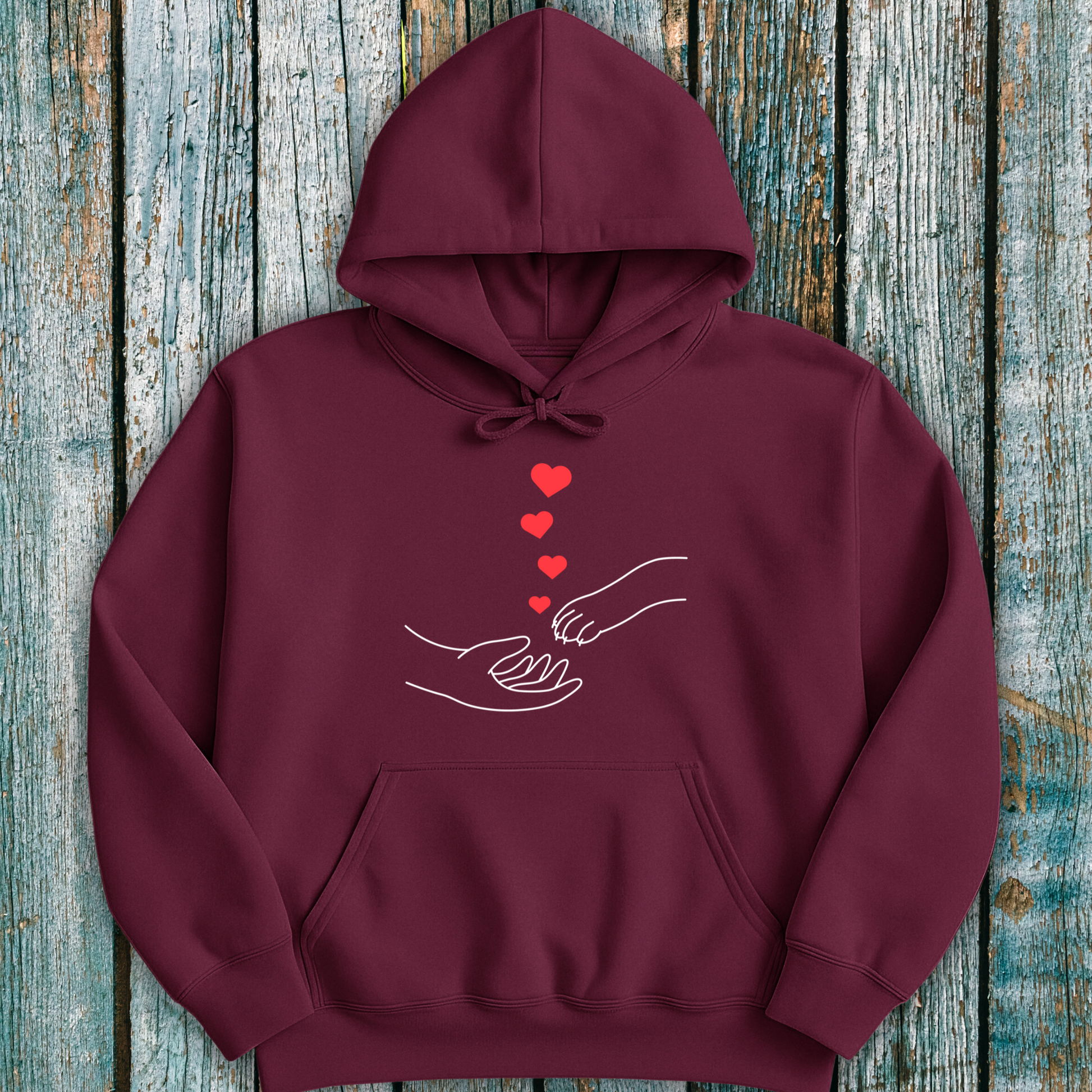 Maroon hoodie with a design of hands holding paws and hearts on a wooden surface