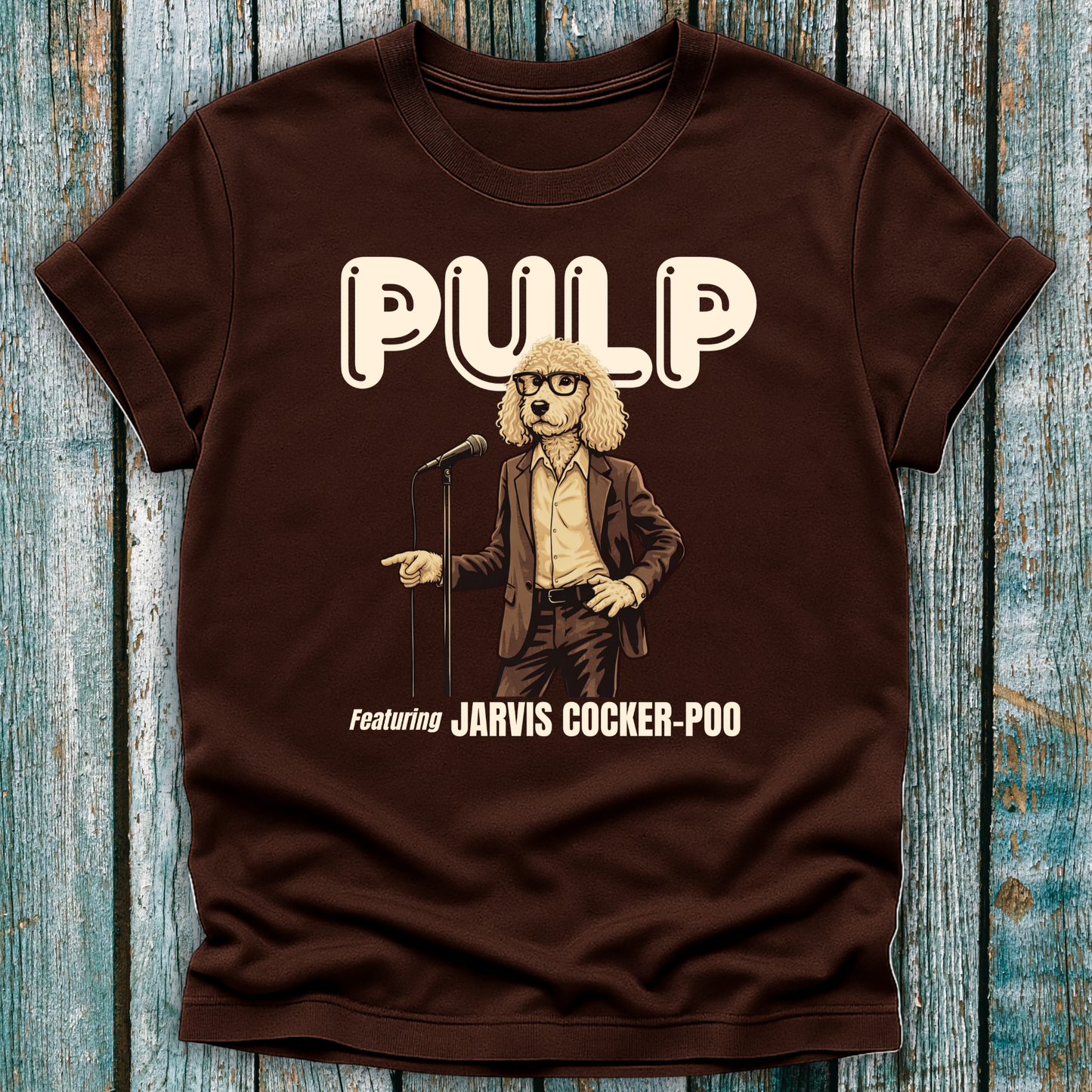 Brown t-shirt with a graphic of a dog in a suit and glasses, holding a microphone, and the text 'PULP featuring Jarvis Cocker Poo' on a wooden surface.