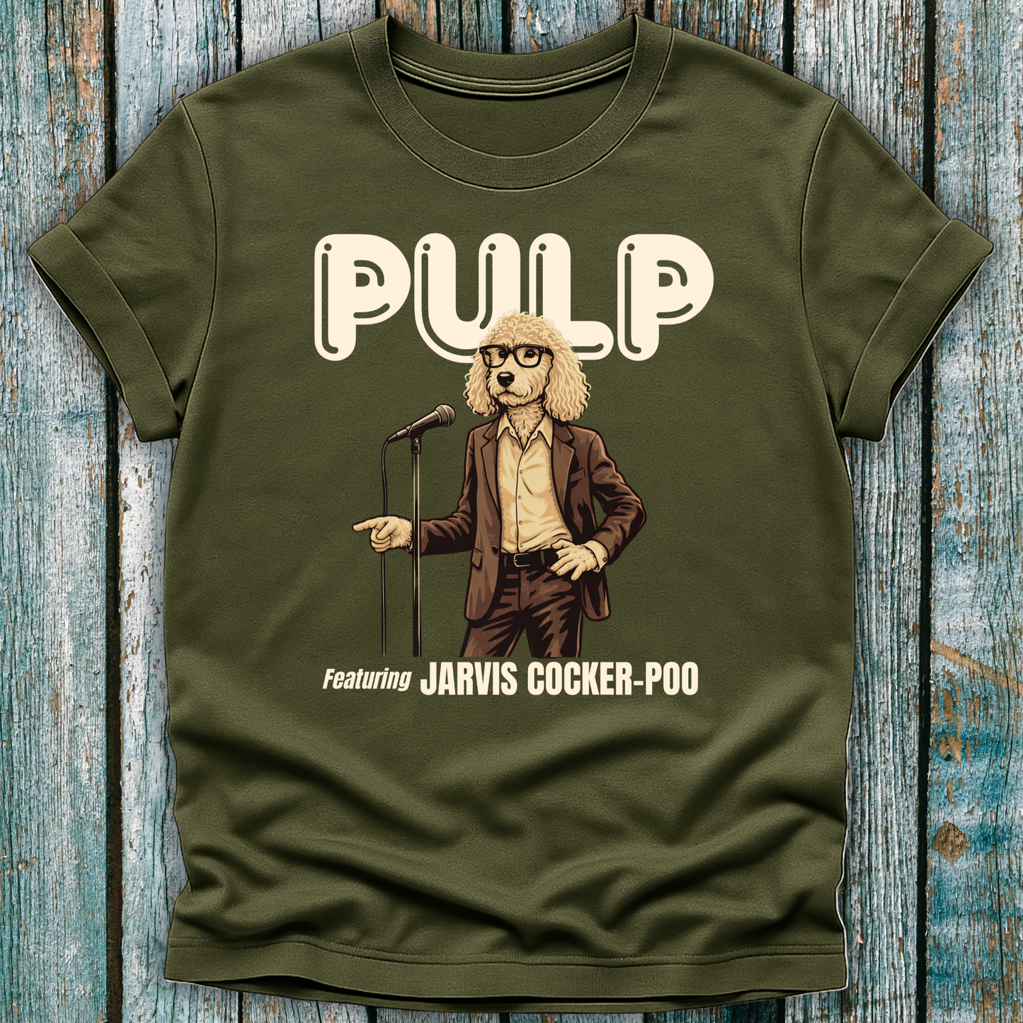 Green t-shirt with a graphic of a dog in a suit and glasses, holding a microphone, with 'Pulp' and 'Jarvis Cocker Poo' text on a wooden surface.