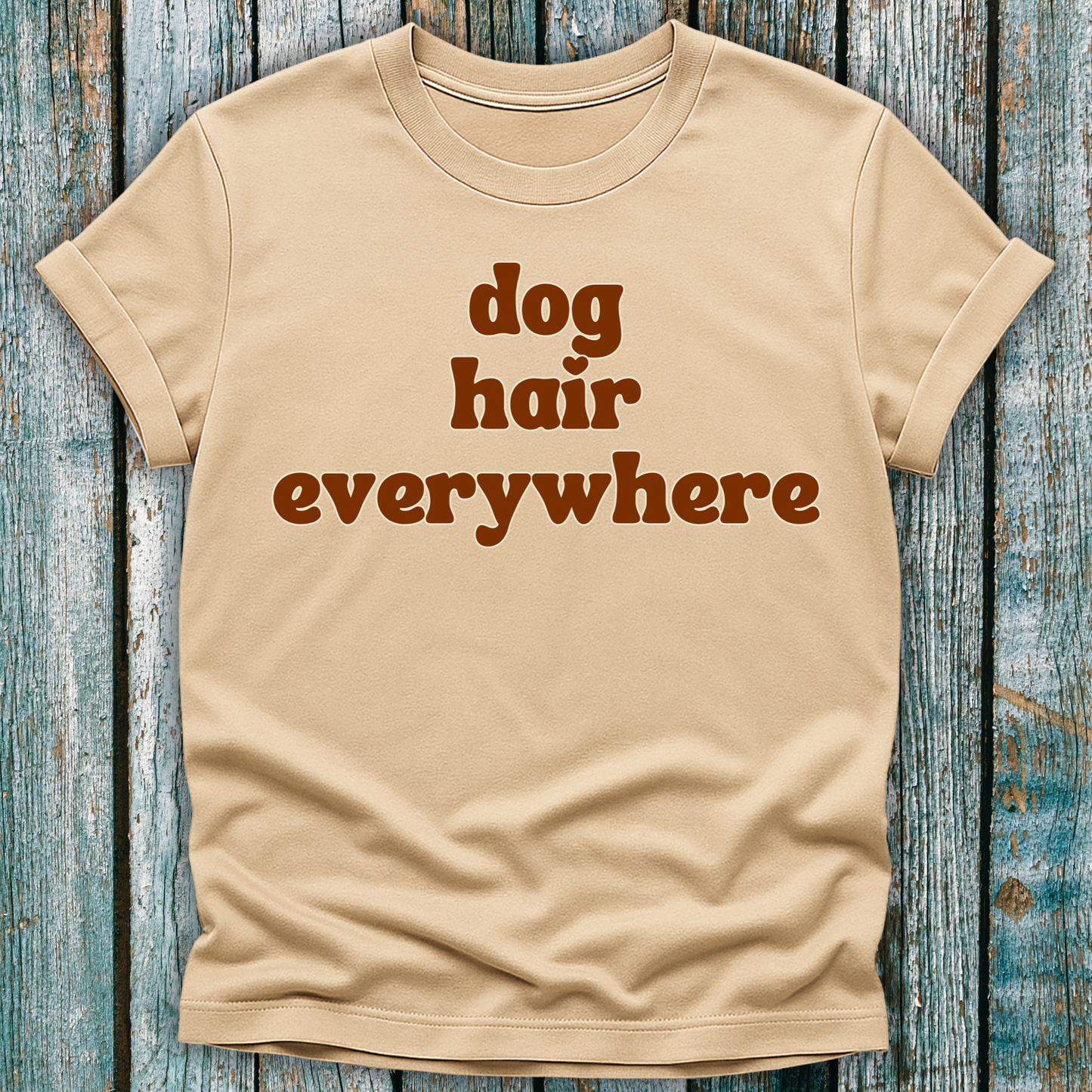 Beige t-shirt with 'dog hair everywhere' text on a wooden surface