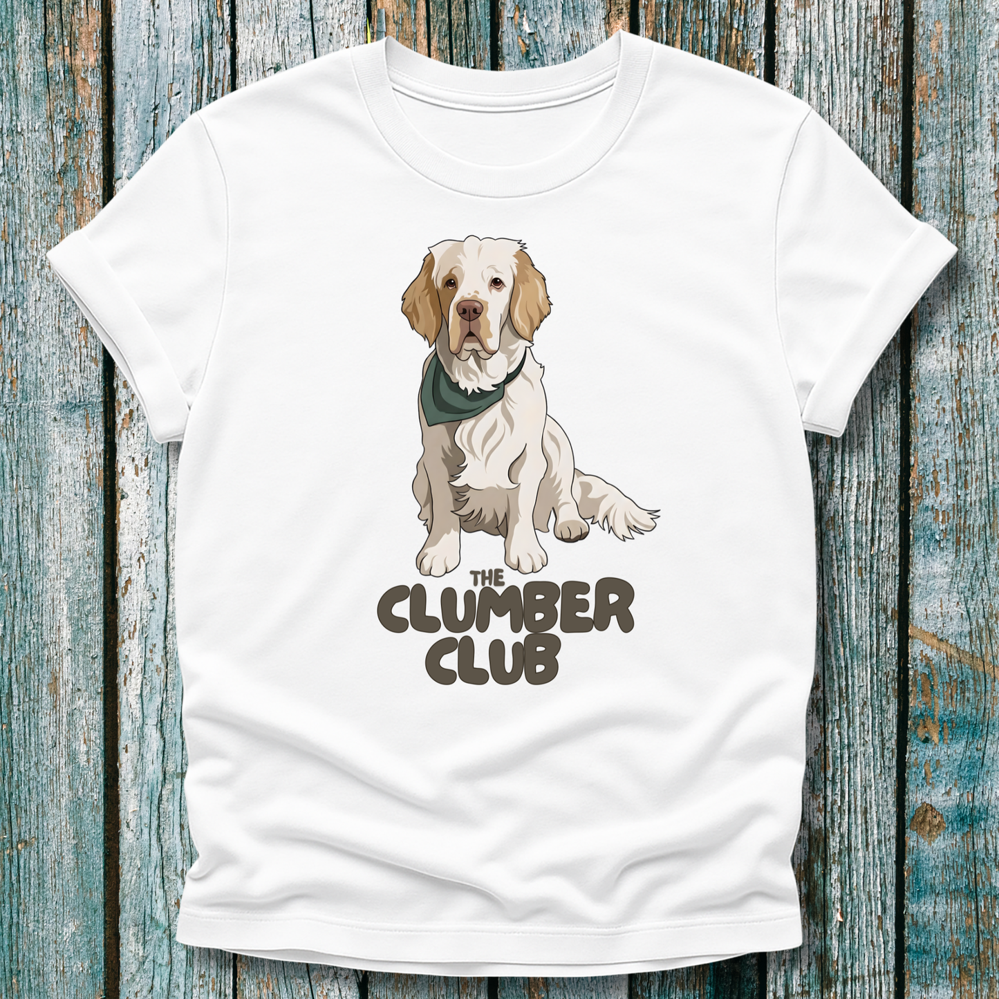 White t-shirt with a Clumber Spaniel graphic and 'The Clumber Club' text on a wooden surface