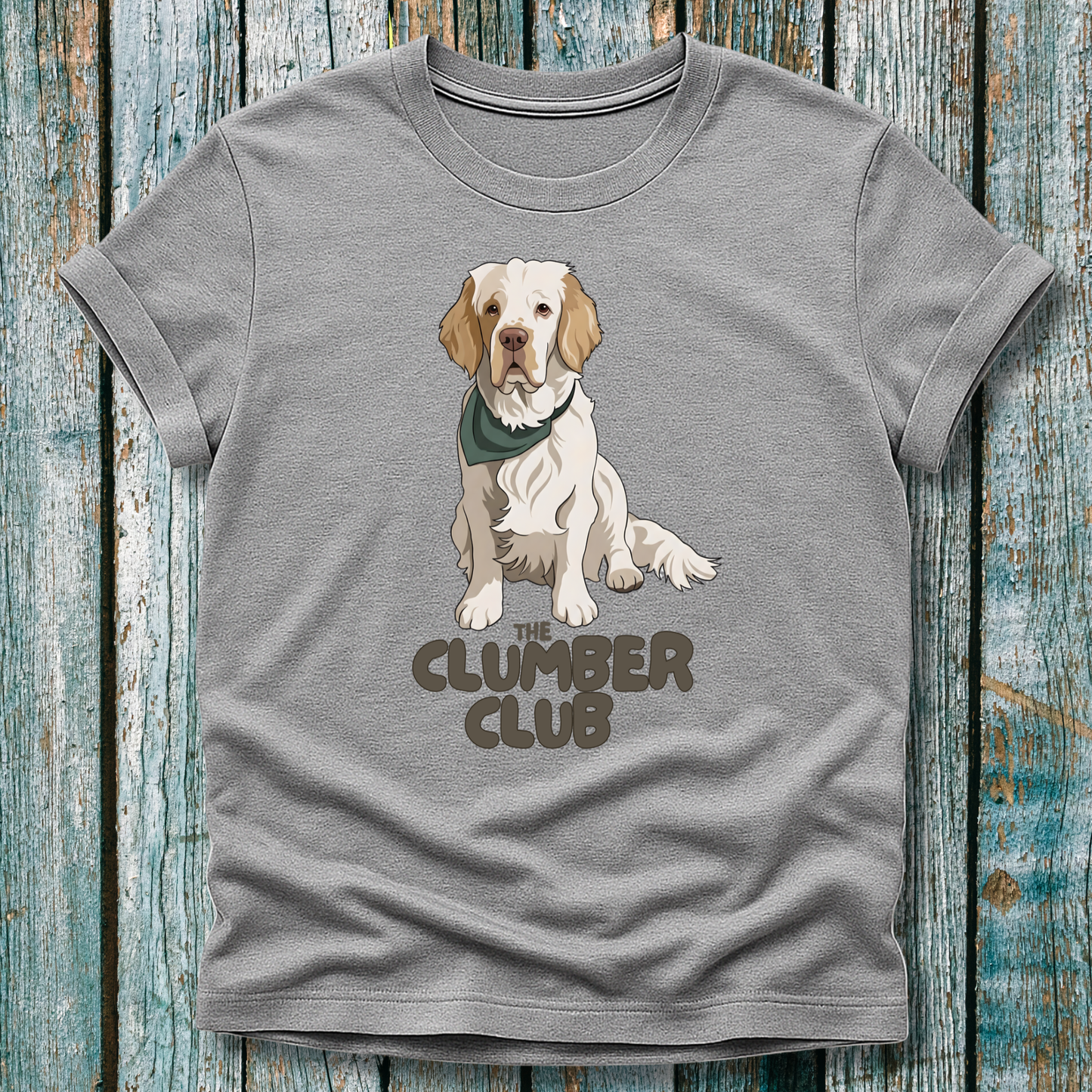 Gray t-shirt with a Clumber Spaniel graphic and 'The Clumber Club' text on a wooden surface