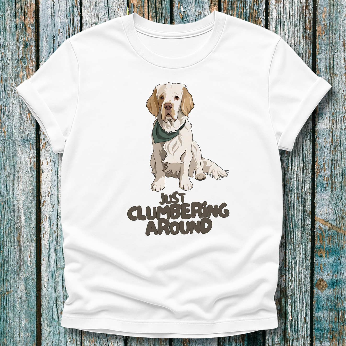 White t-shirt with a Clumber Spaniel graphic and text 'Just Clumbering Around' on a wooden surface