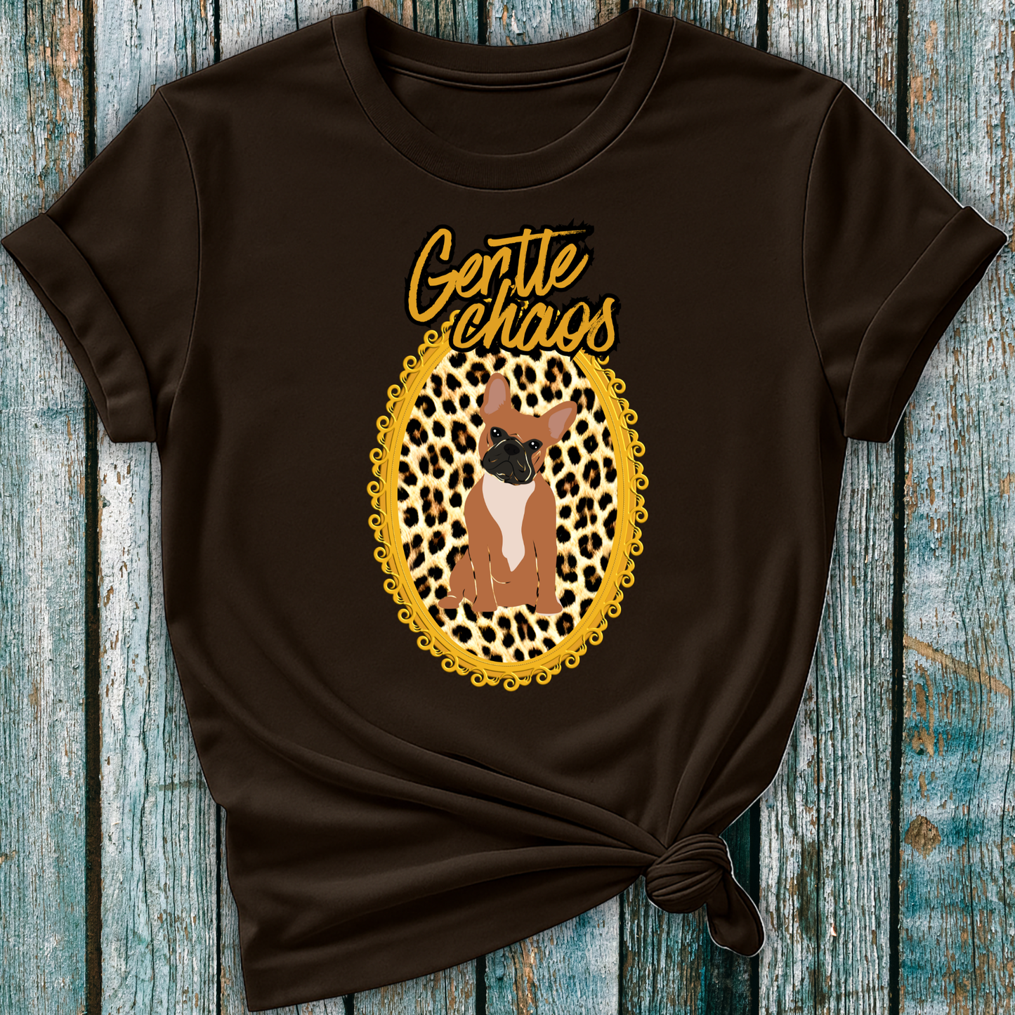 Brown t-shirt with a graphic of a Frenchie dog in a leopard print frame and 'Gentle Chaos' text, on a wooden surface.