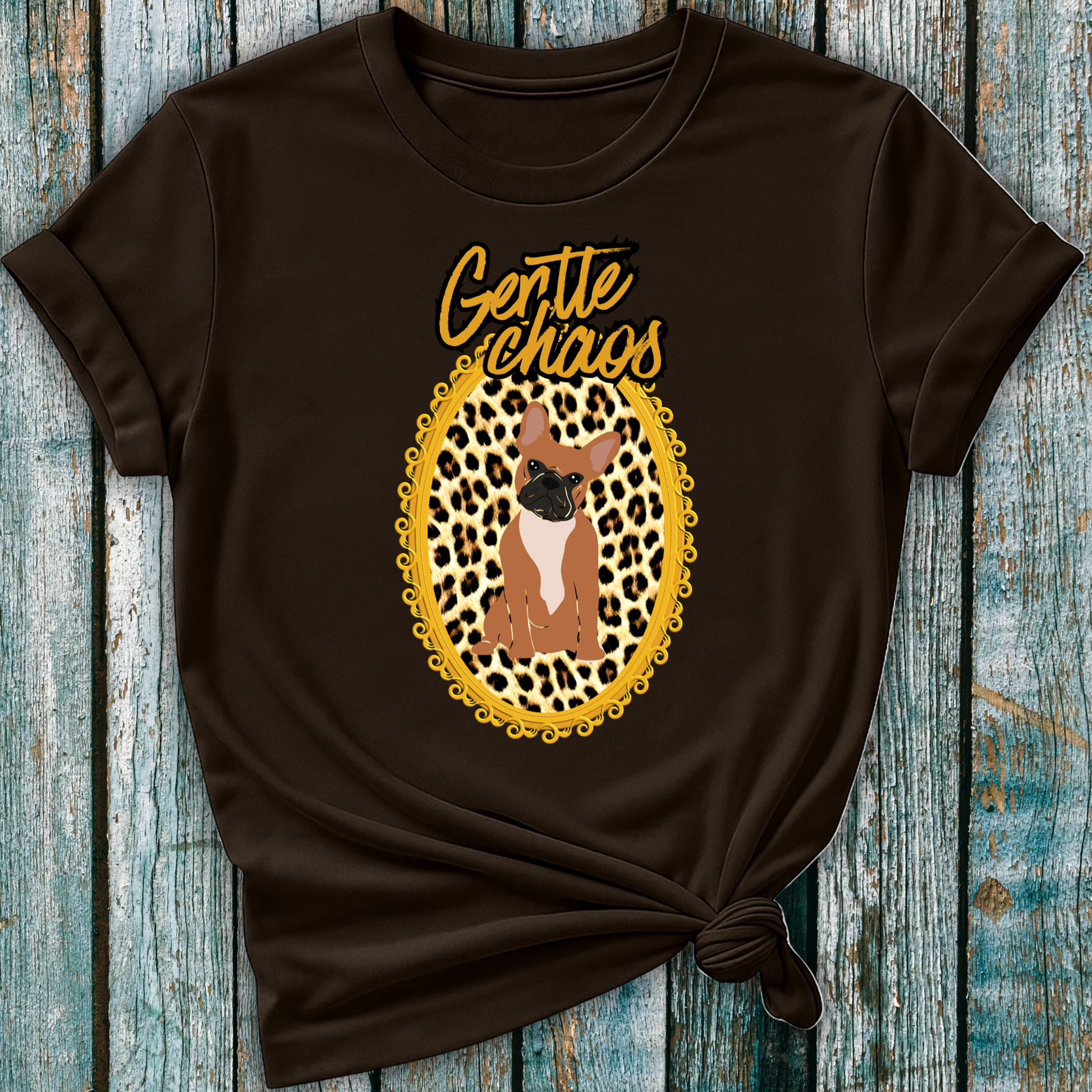 Brown t-shirt with a graphic of a Frenchie dog in a leopard print frame and 'Gentle Chaos' text, on a wooden surface.