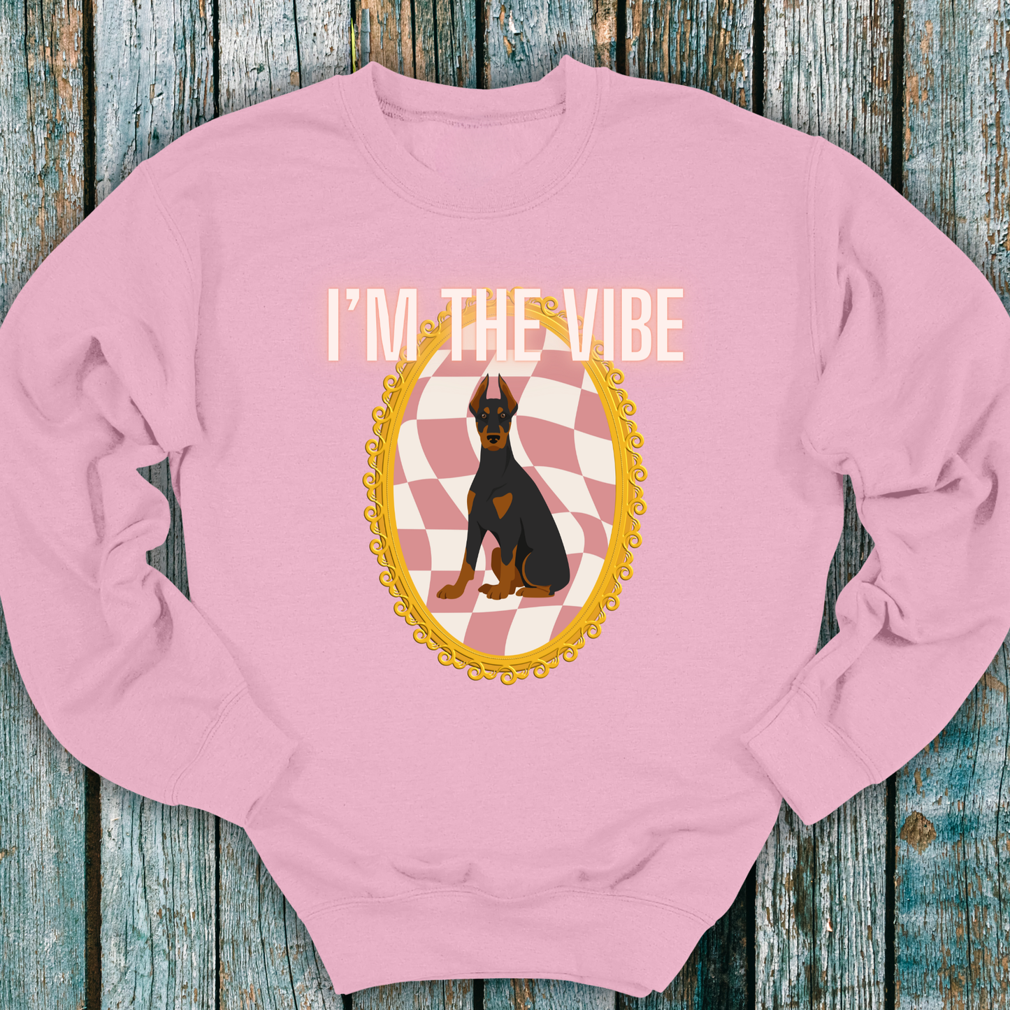 Pink sweatshirt with a Doberman dog graphic and 'I'm the Vibe' text on a wooden surface