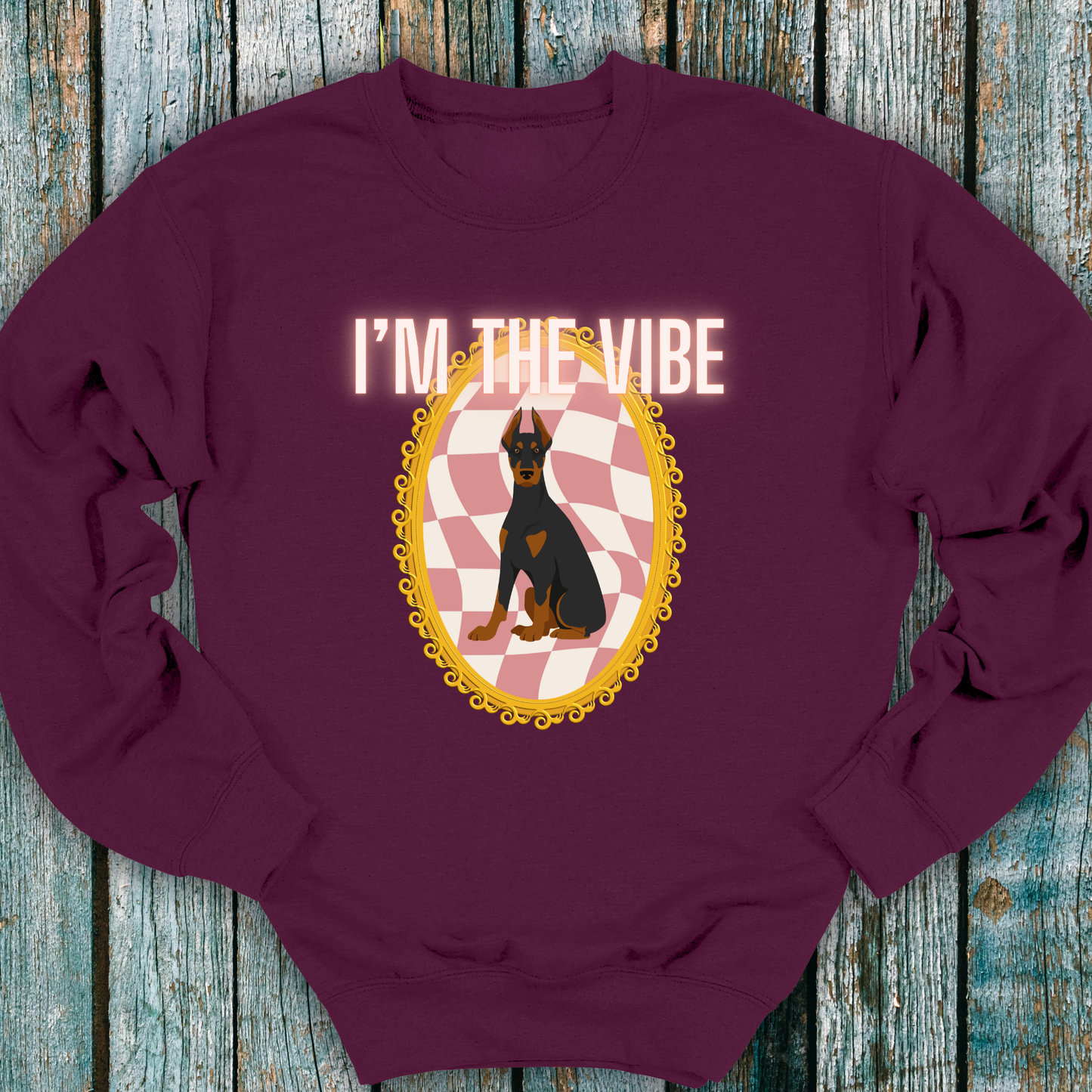 Maroon sweatshirt with a graphic of a Doberman dog and 'I'm the Vibe' text on a wooden surface