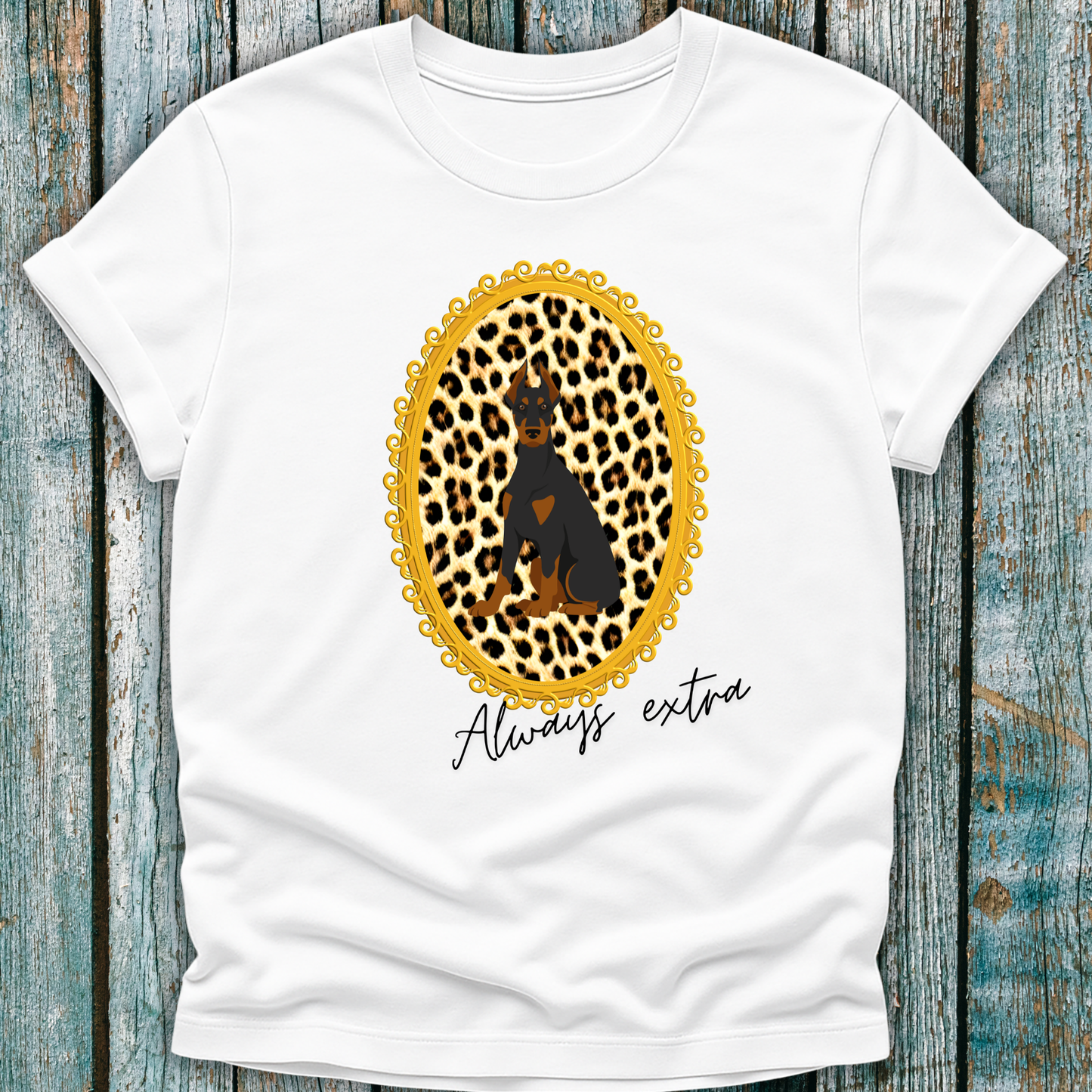 White t-shirt with a leopard print, a Doberman dog and "always extra" text on a wooden surface