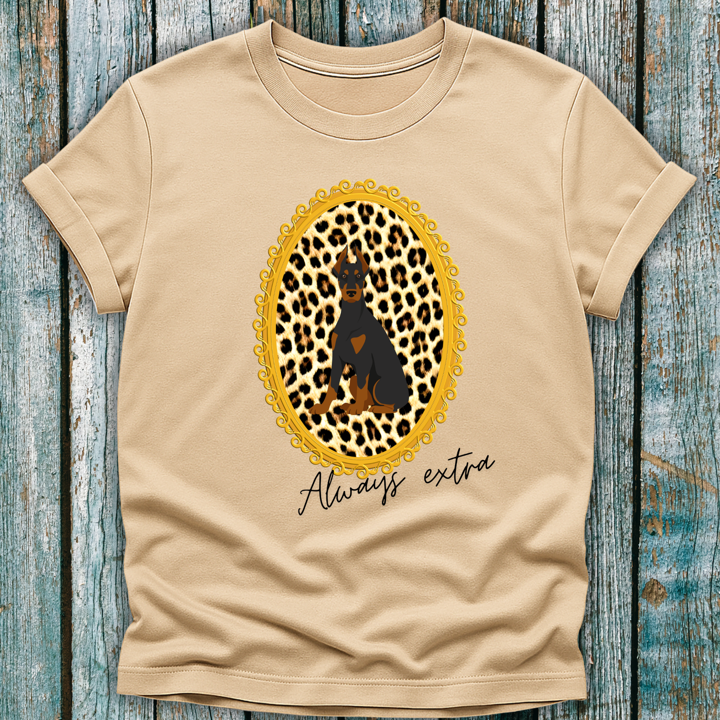 Beige t-shirt with a leopard print design, a Doberman dog and "always extra" text on a wooden surface