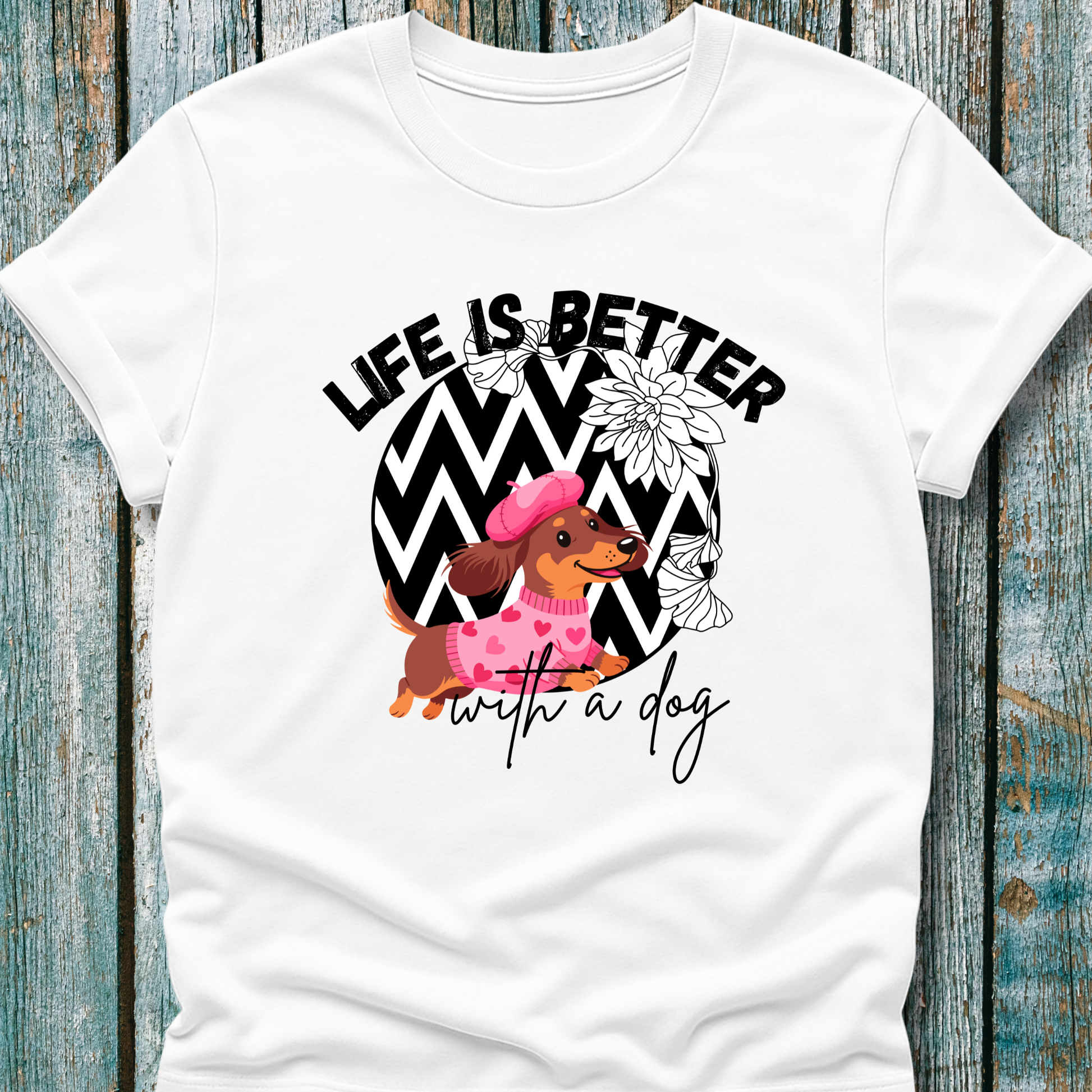 White t-shirt with a dachshund graphic and 'Life is better with a dog' text on a wooden surface.