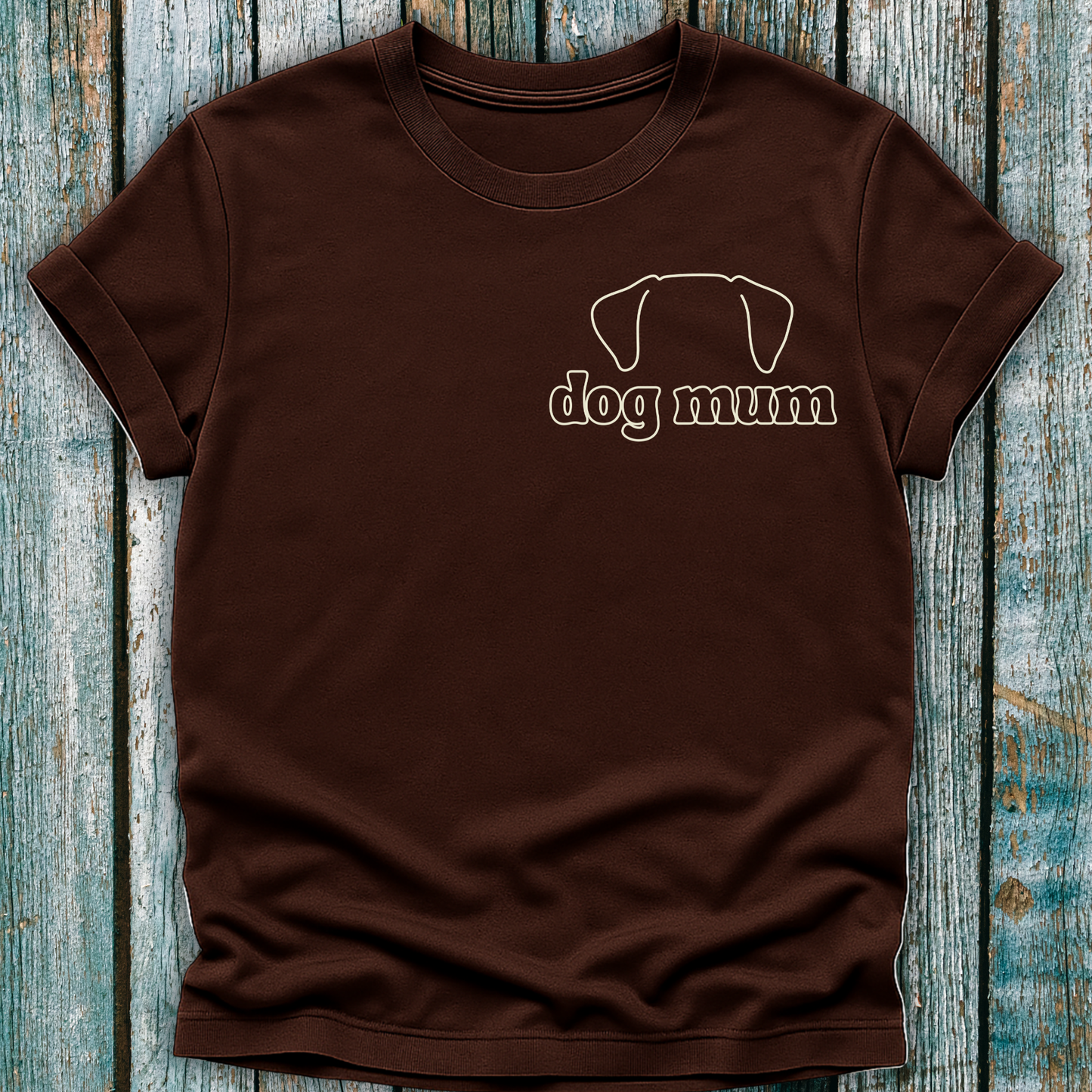 Brown t-shirt with 'dog mum' text and dog silhouette on a wooden surface
