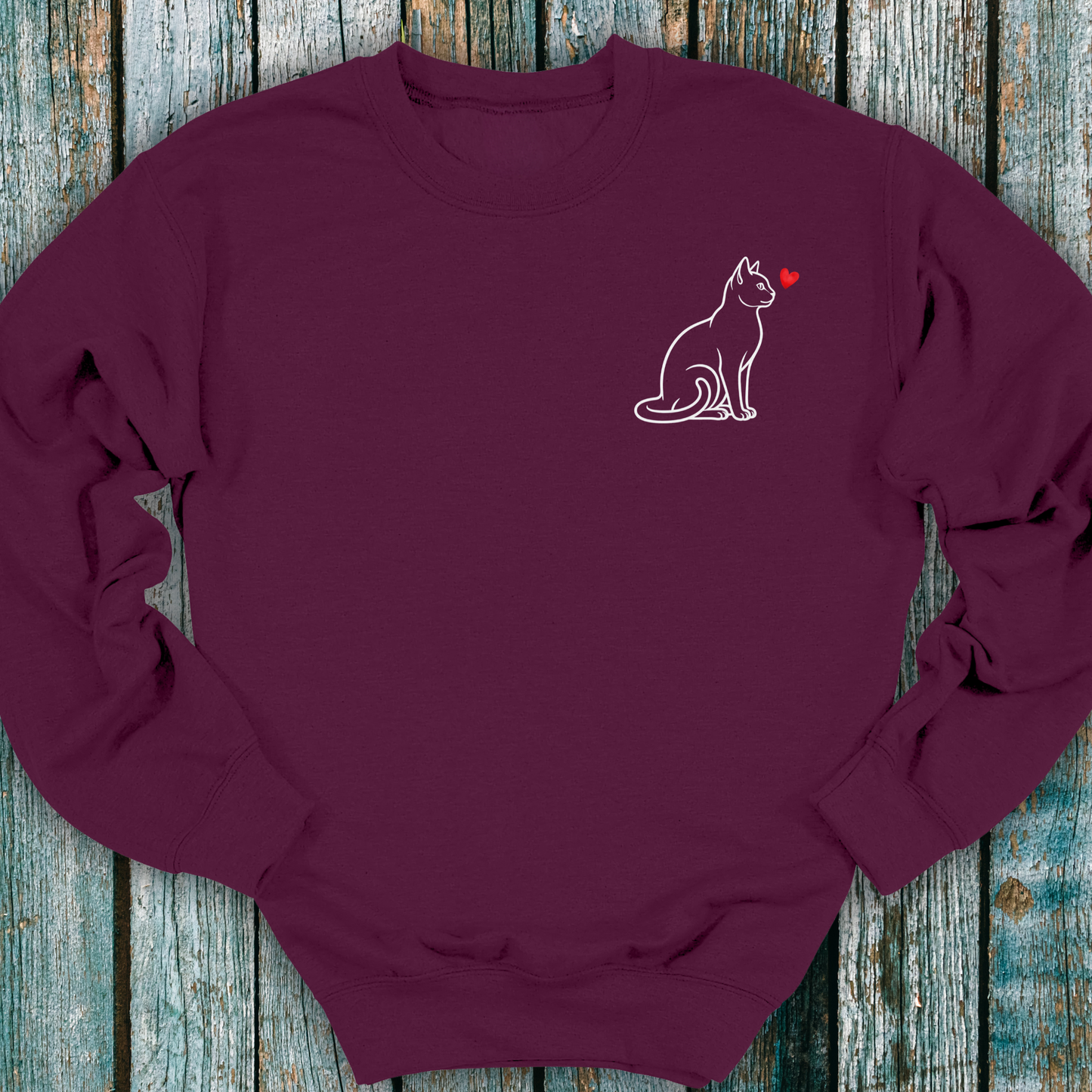Maroon sweatshirt with a cat and heart design on a wooden surface