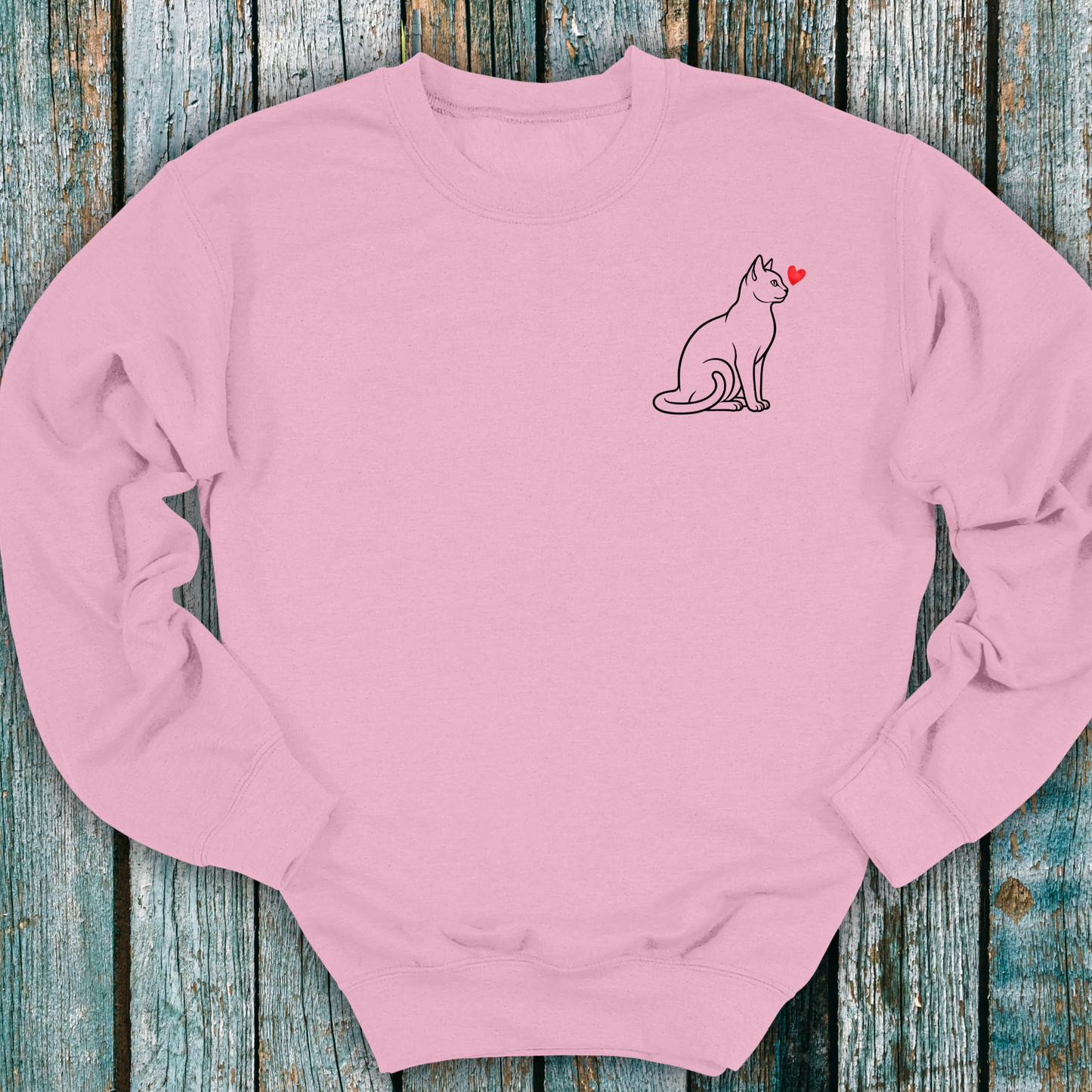 Pink sweatshirt with a cat and heart design on a wooden surface
