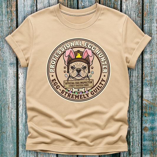 Beige t-shirt with a graphic of a dog wearing an egg hunter hat on a wooden surface