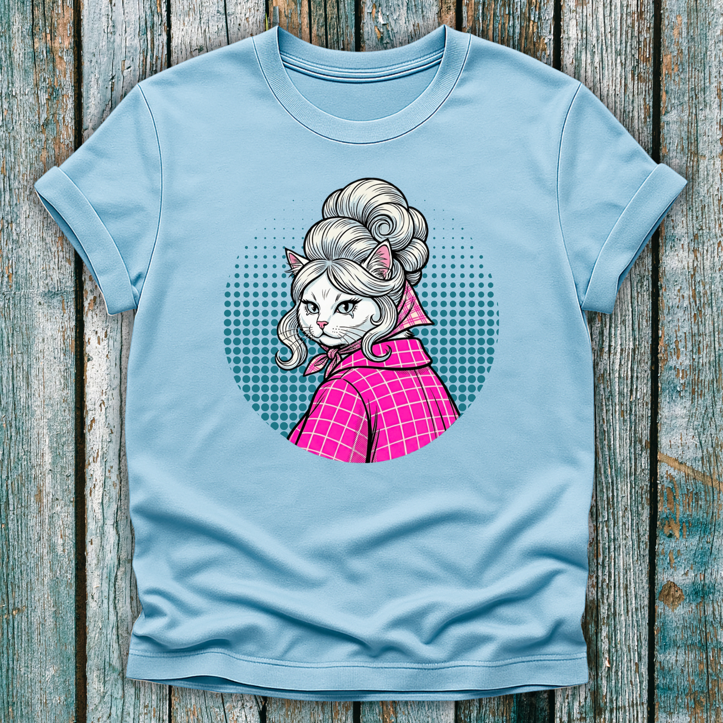 Light Blue  t-shirt with a colorful graphic of a pop art cat character in a pink outfit on a wooden surface