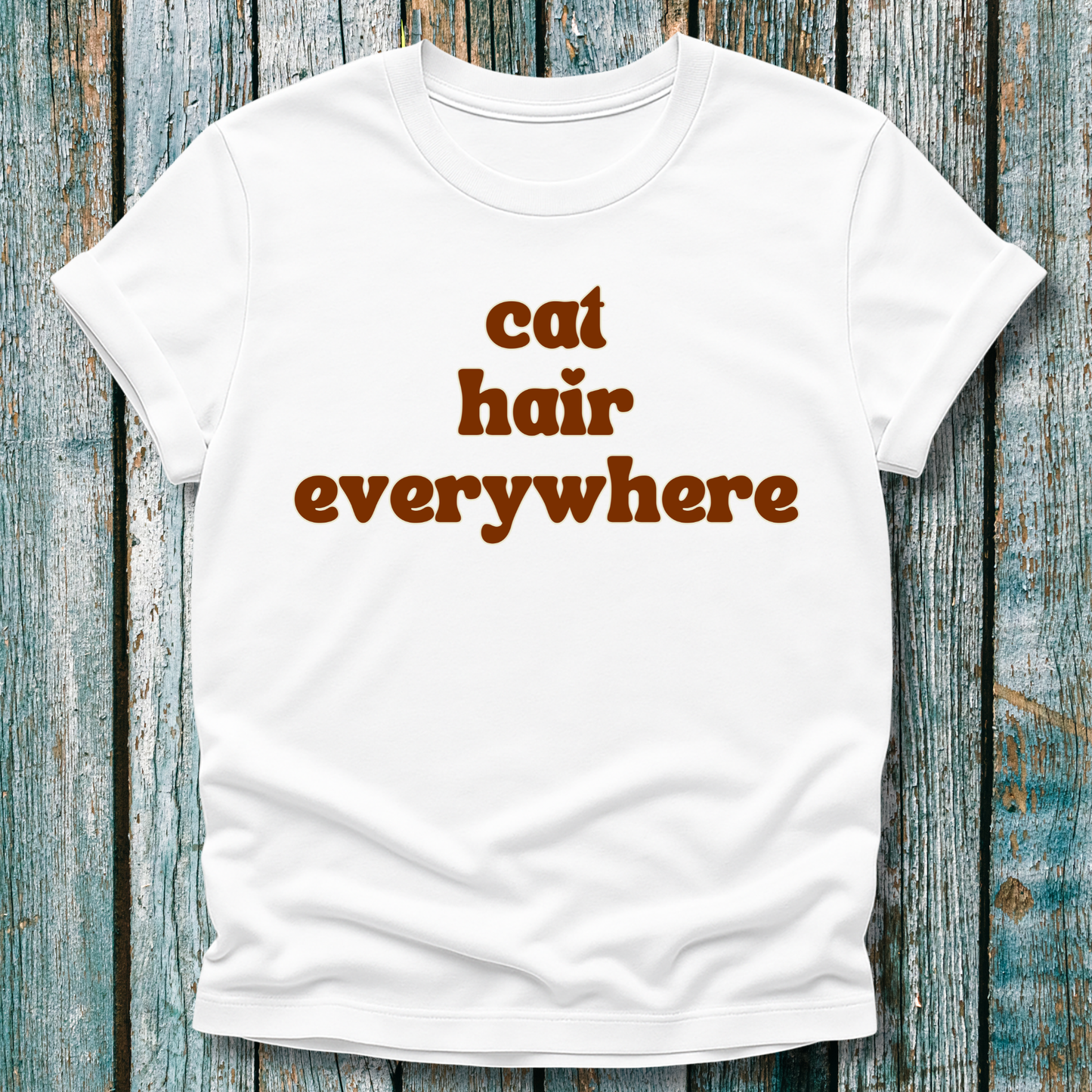 White t-shirt with 'cat hair everywhere' text on a wooden background