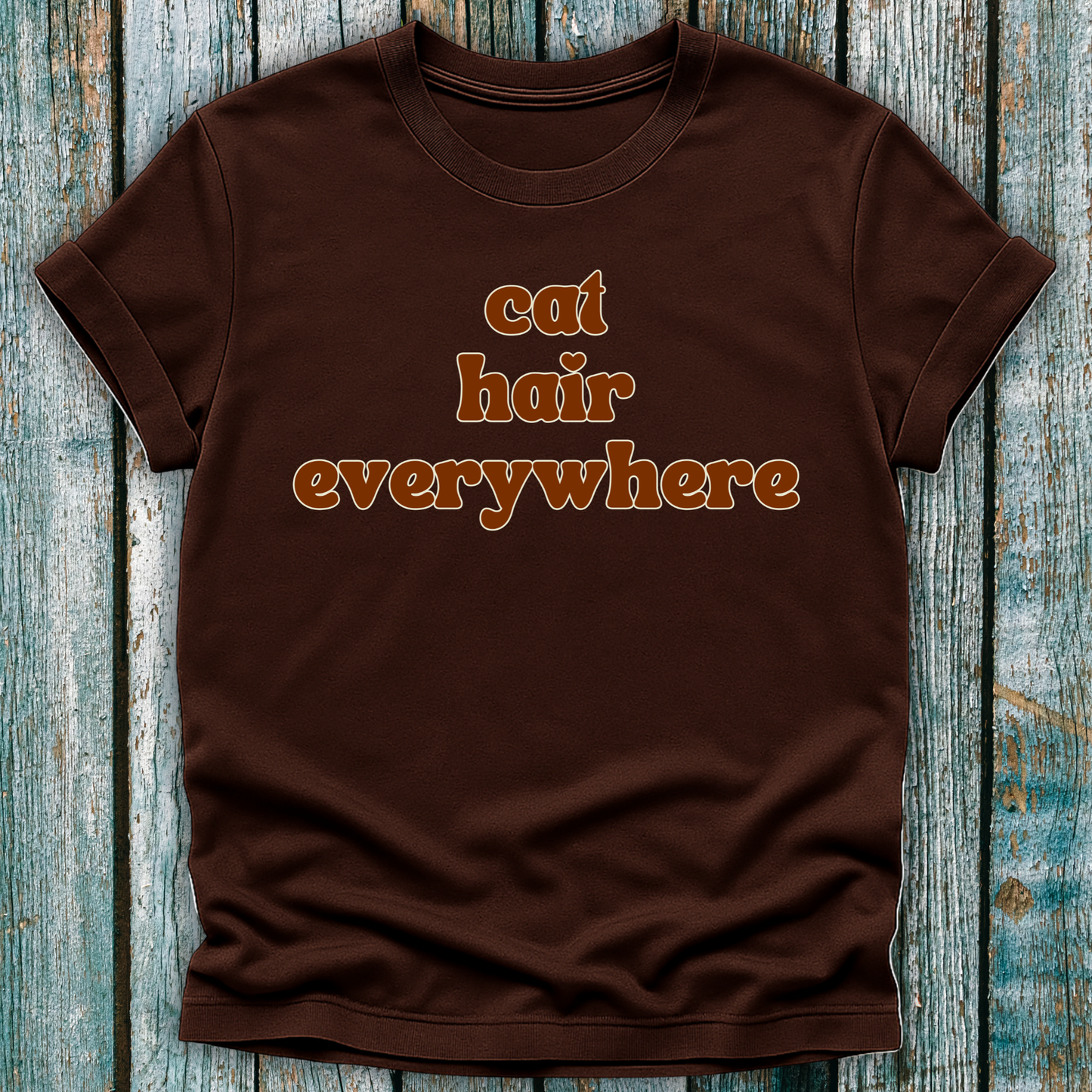 Brown t-shirt with 'cat hair everywhere' text on a wooden surface