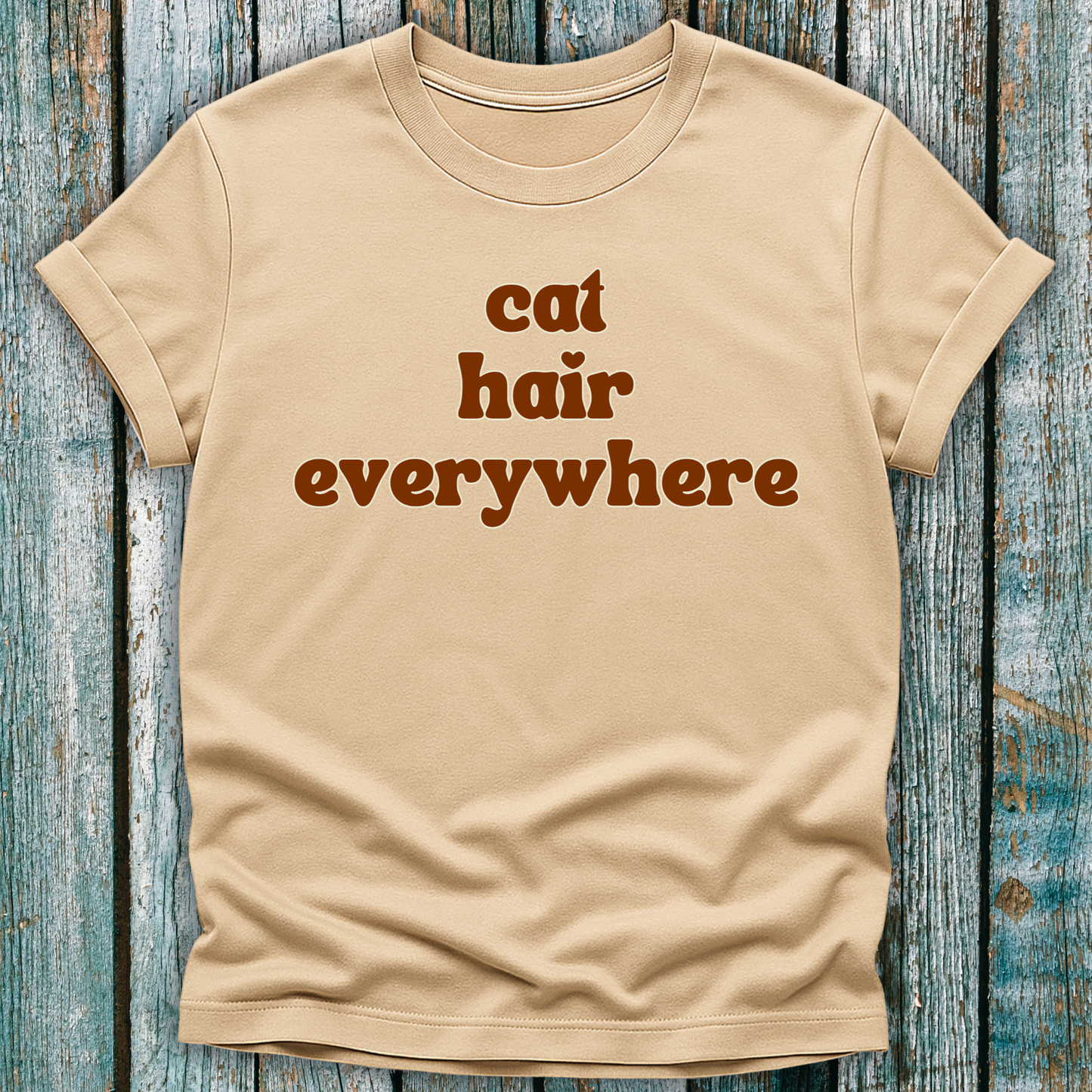 Beige t-shirt with 'cat hair everywhere' text on a wooden surface