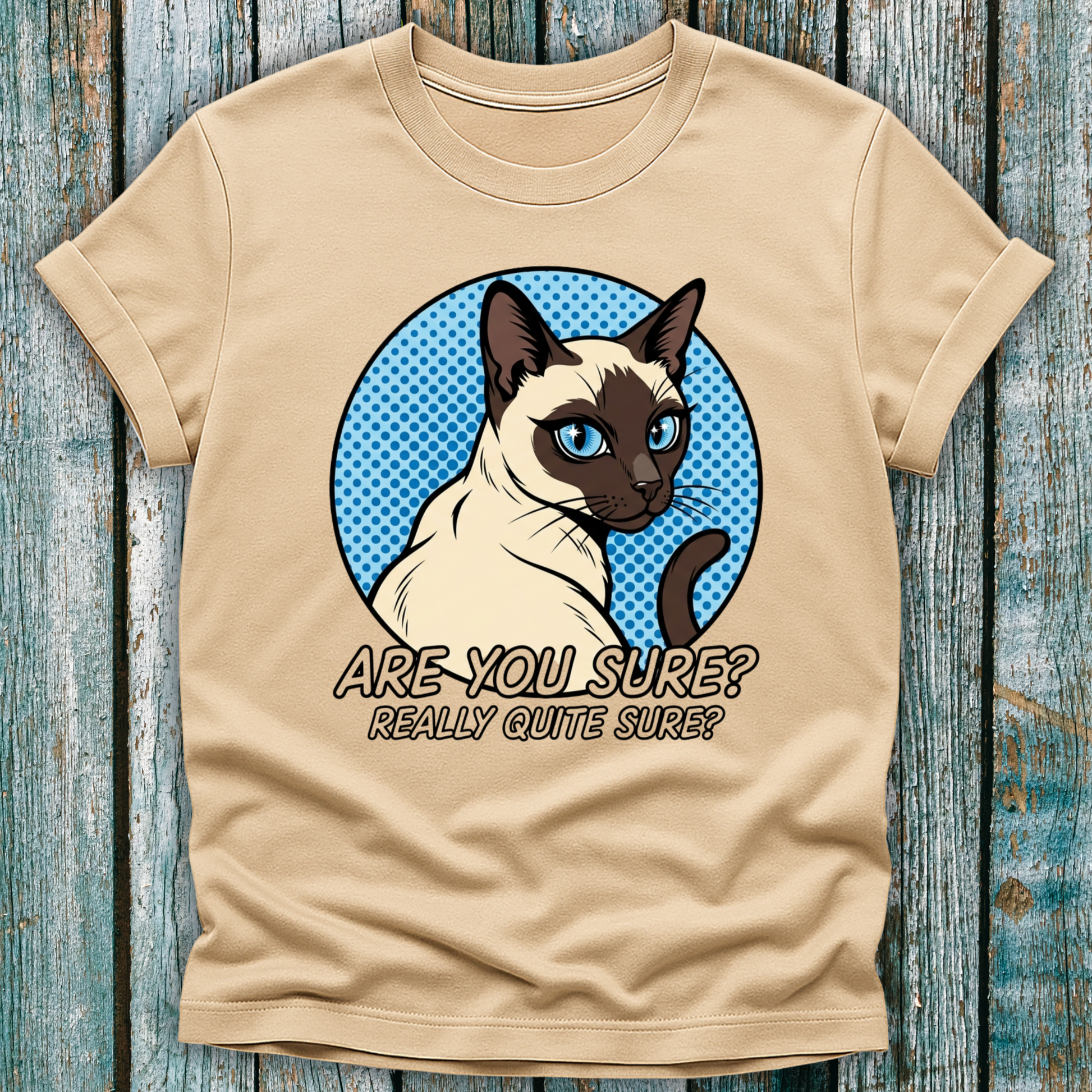 Beige t-shirt with a Siamese cat graphic and text on a wooden surface