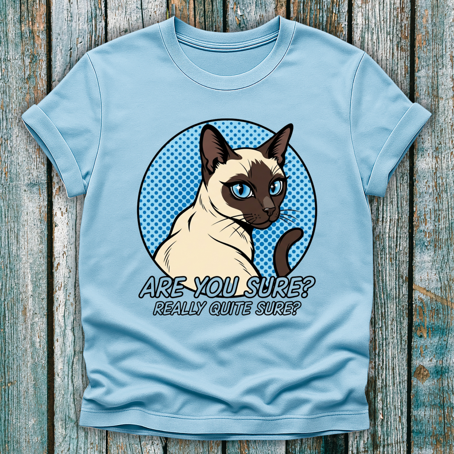 Light blue t-shirt with a Siamese cat graphic and text on a wooden surface