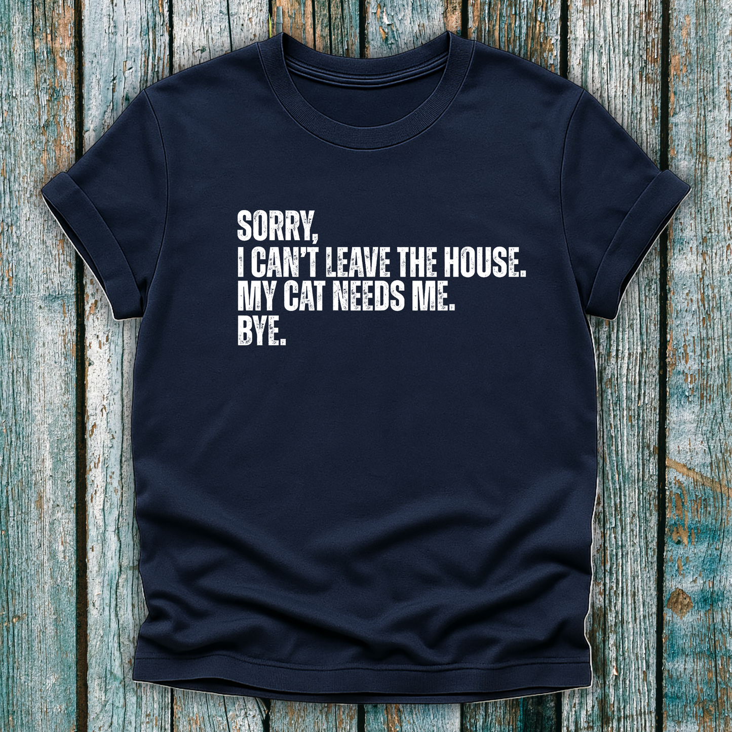 Navy t-shirt with white text "Sorry' I can't leave the house. My cat needs me. Bye." on a wooden background