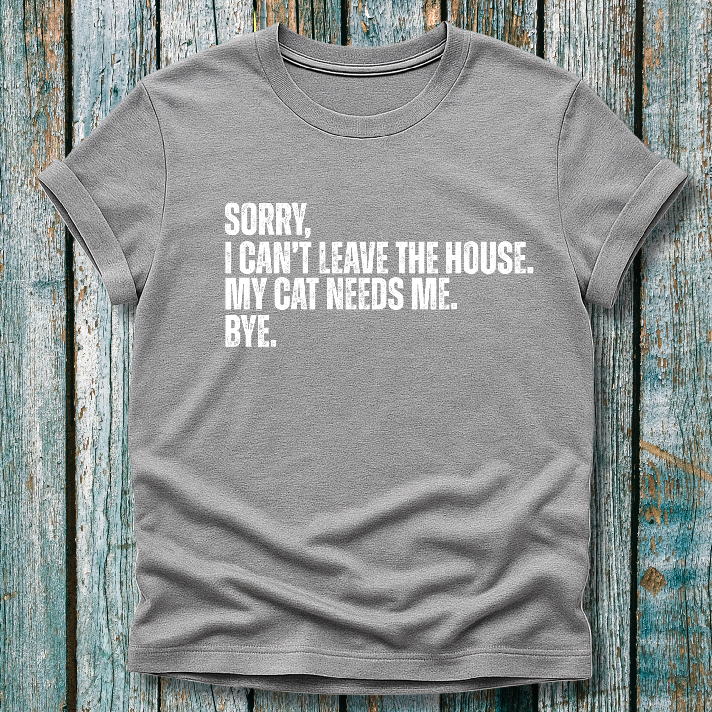 Gray t-shirt with white text "Sorry' I can't leave the house. My cat needs me. Bye." on a wooden background