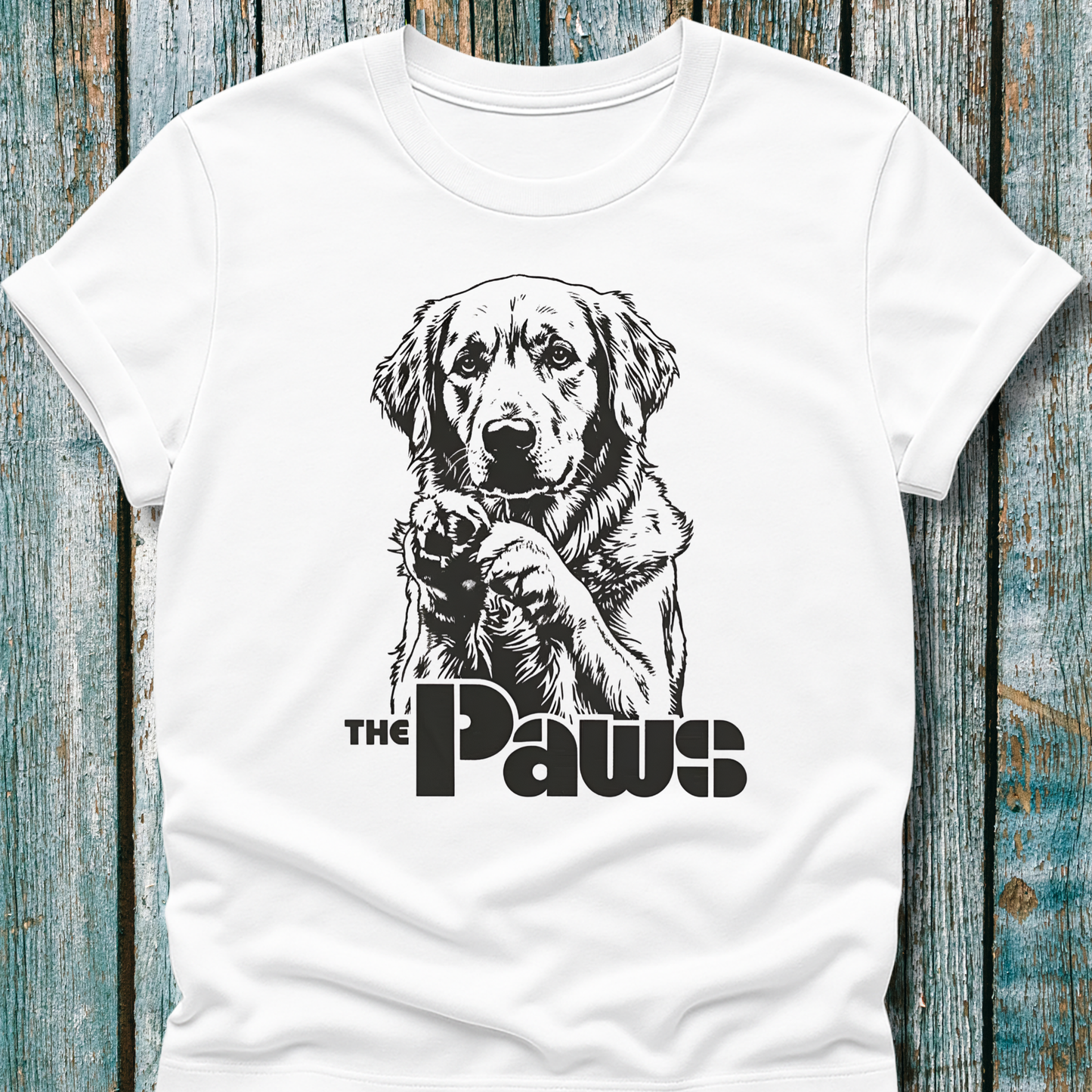 White t-shirt with a dog graphic and 'The Paws' text on a wooden surface