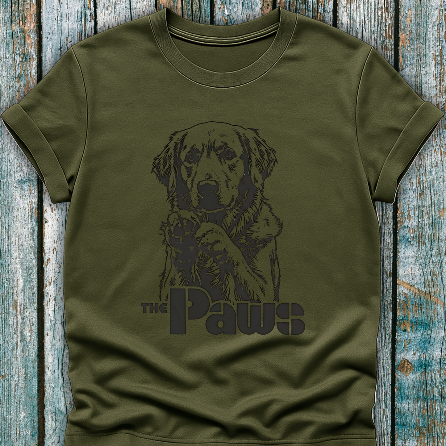 Green t-shirt with a dog graphic and 'The Paws' text on a wooden surface