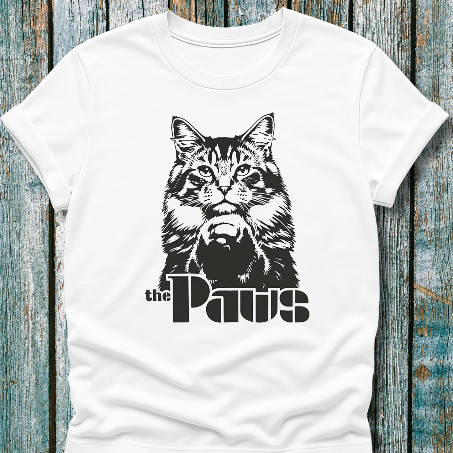 White t-shirt with a black cat graphic and 'the Paws' text on a wooden surface