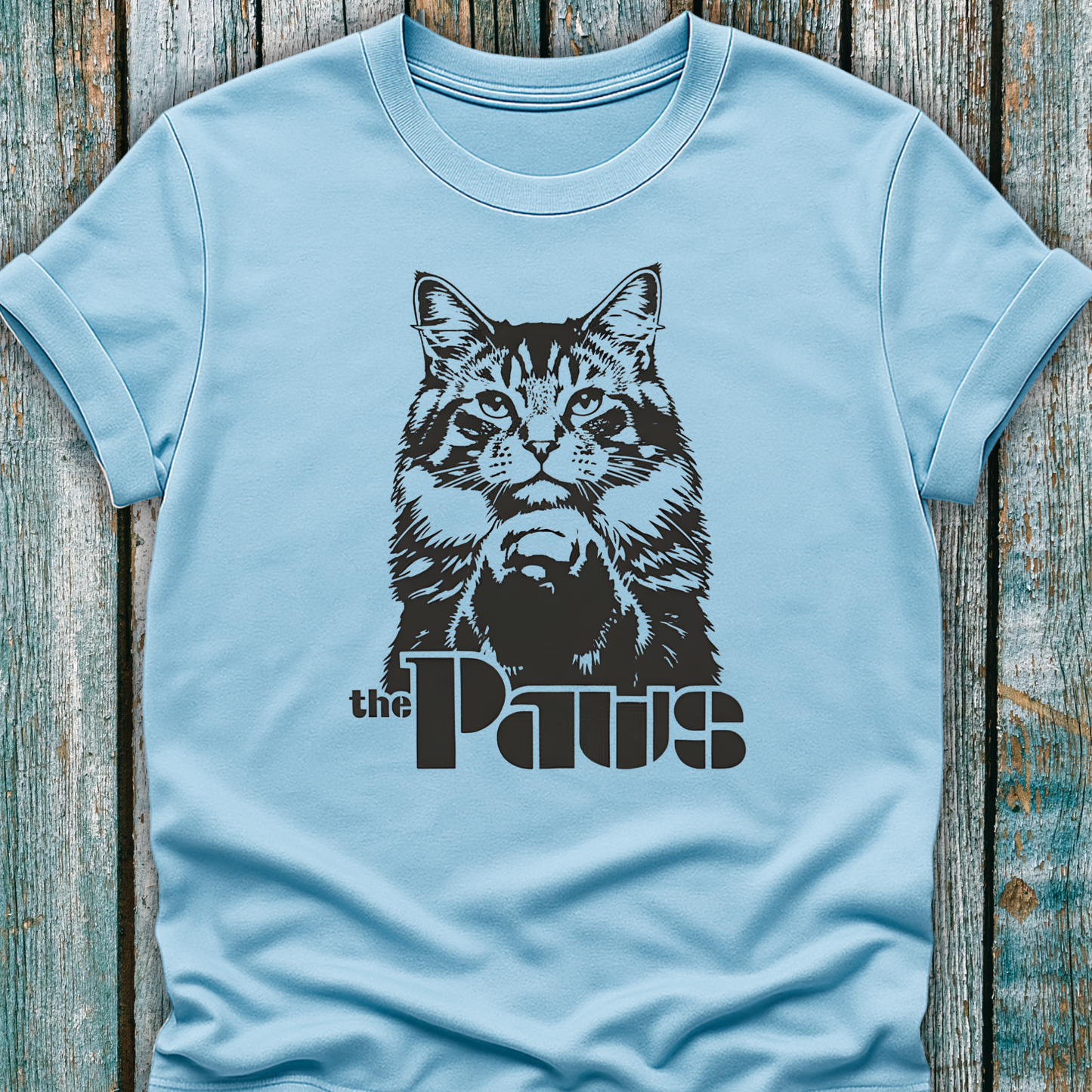 Light blue t-shirt with a black cat graphic and 'the Paws' text on a wooden surface